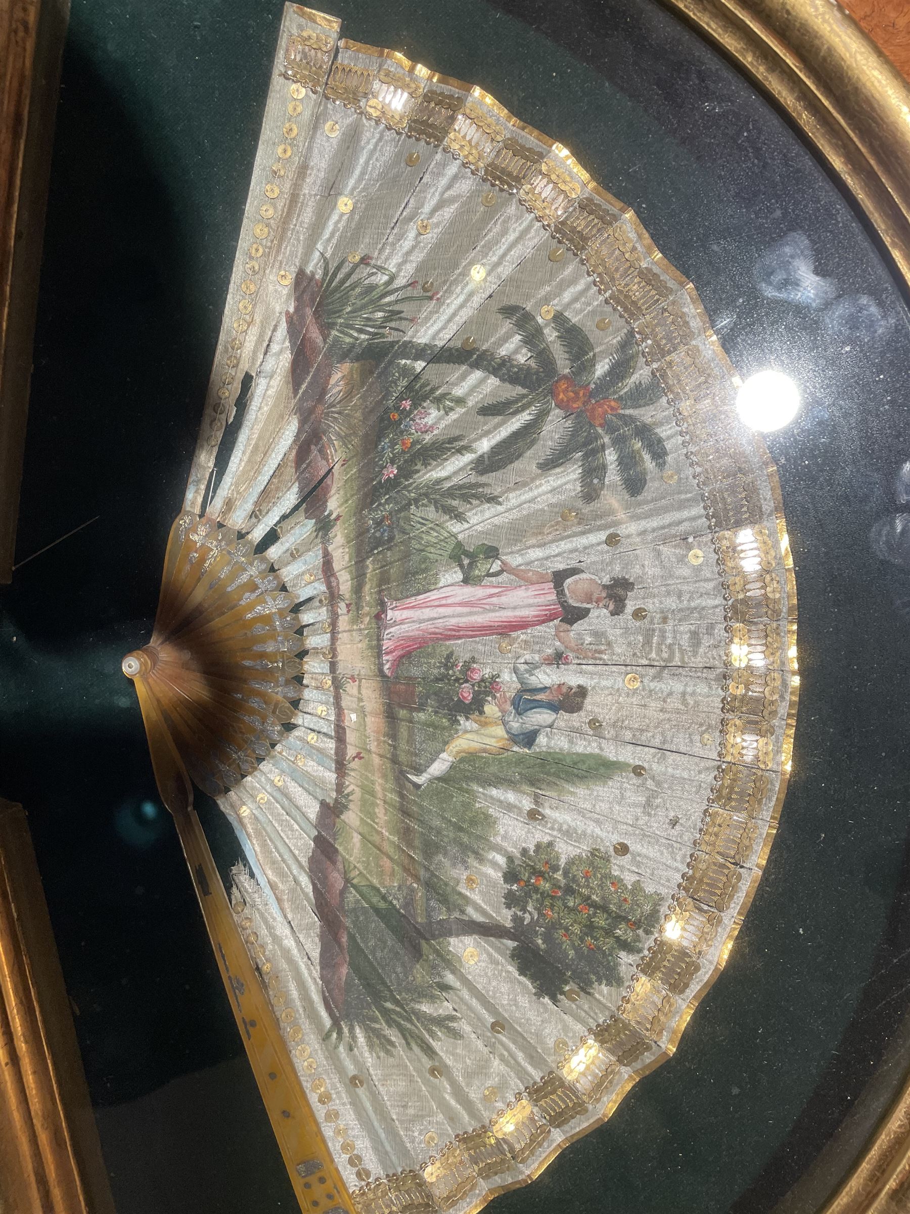 18th century fan, the horn sticks and guard with silvered and gilded decoration, the silk leaf painted in strong colours with a young couple in a garden setting, within a border of gold coloured sequins, framed and glazed, overall H35cm L55cm
Provenance: From the Estate of the late Dowager Lady St Oswald