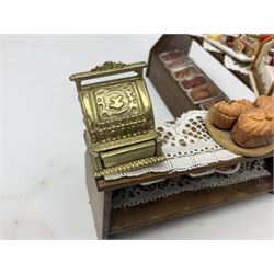 Collection of miniature dolls house grocery shop furniture and produce, comprising glazed corner counter with brass style cash register, shelved preserves unit, pies, cheese board and trays of meats, pair of white cheese counters, biscuit display with six tins, glazed preserves cabinet, pair of shop chairs and four further cheese boards complete with grapes and label flags