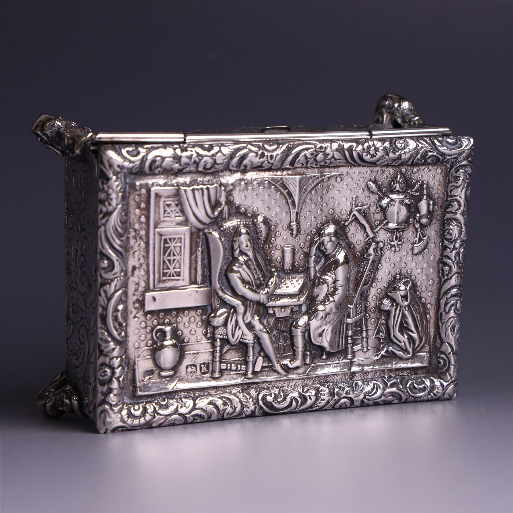 Victorian silver tobacco box, rectangular form, hinged lid embossed with a gaming scene, the body engraved with scrolls and flowers, upon four scrolling mask feet, hallmarked George Heath London 1885, H4.5cm, W10.5cm