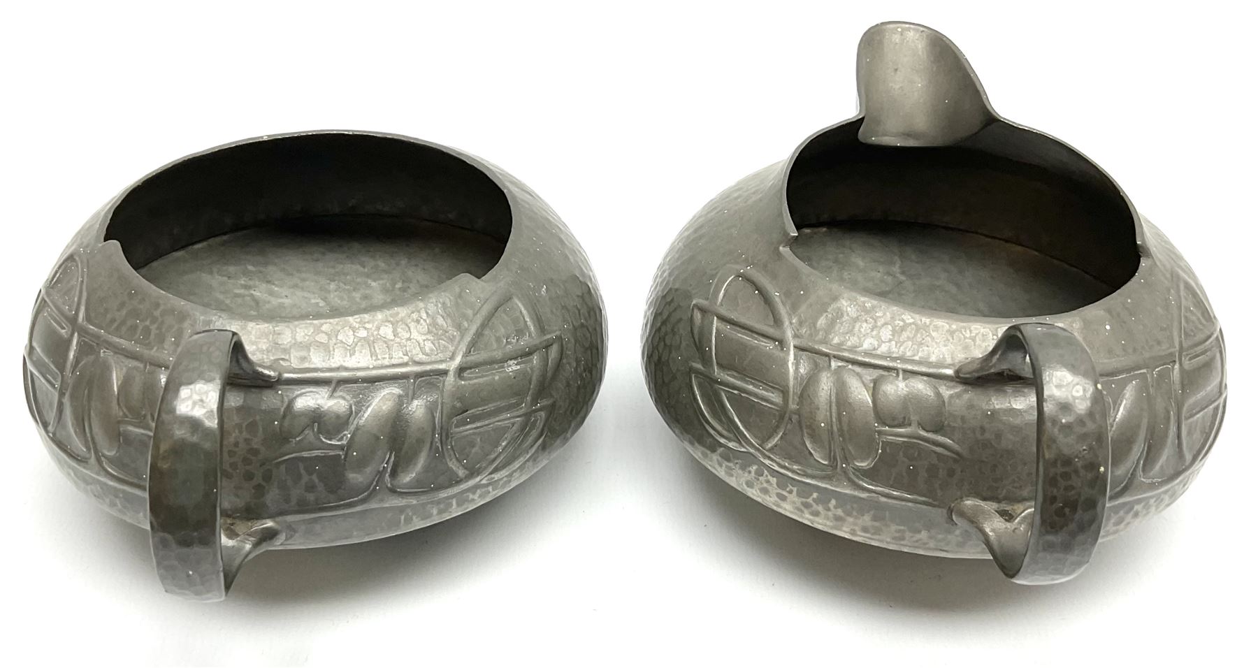 Archibald Knox for Liberty & Co Tudric pewter three piece tea service, comprising teapot with woven reed handle, single handled open sucrier, and milk jug, each with planished finish and detailed with honesty flowers, each impressed beneath Made in England Tudri Pewter 0231 