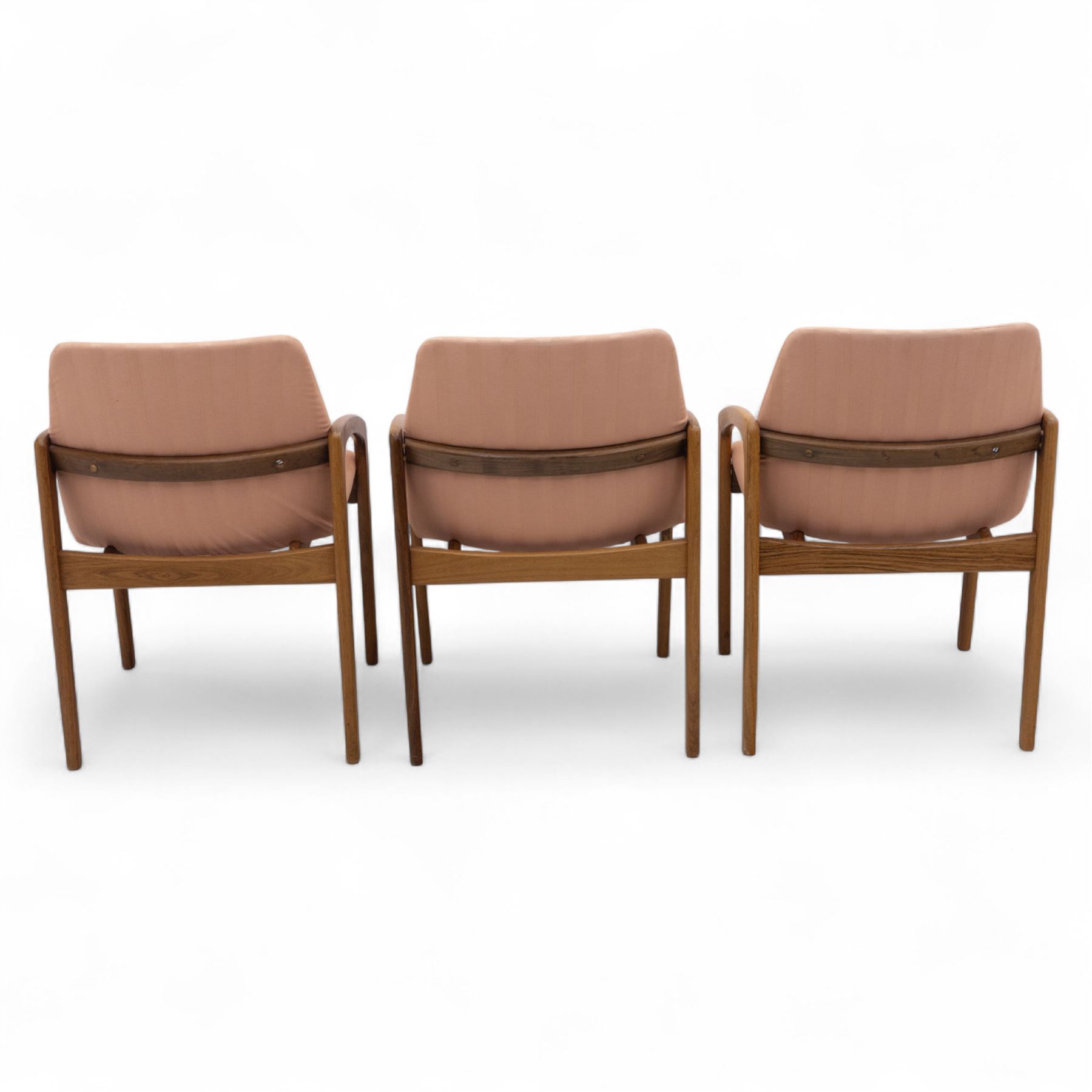 Mid-20th century Danish teak armchairs, each with curved open arms and upholstered seat and backrest in salmon pink striped fabric, raised on tapering legs