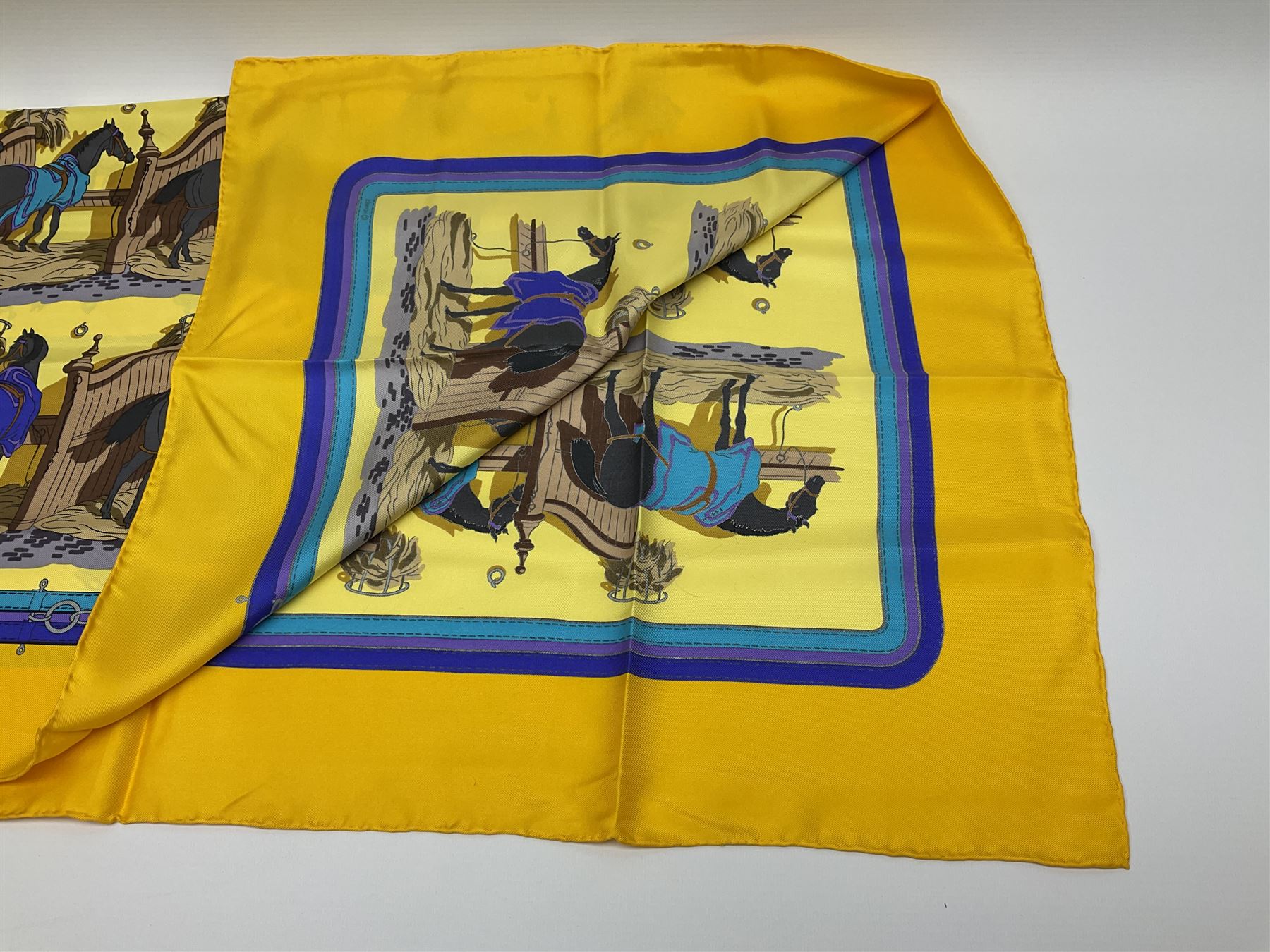 Hermès 'Ecuries' silk scarf, designed by Hugo Grygkar in 1947, printed with twenty horses in their respective stables, on yellow ground contained within stitched effect blue and purple and darker yellow gold borders, with rolled hand stitched edges and Hermes material label, 87cm square
