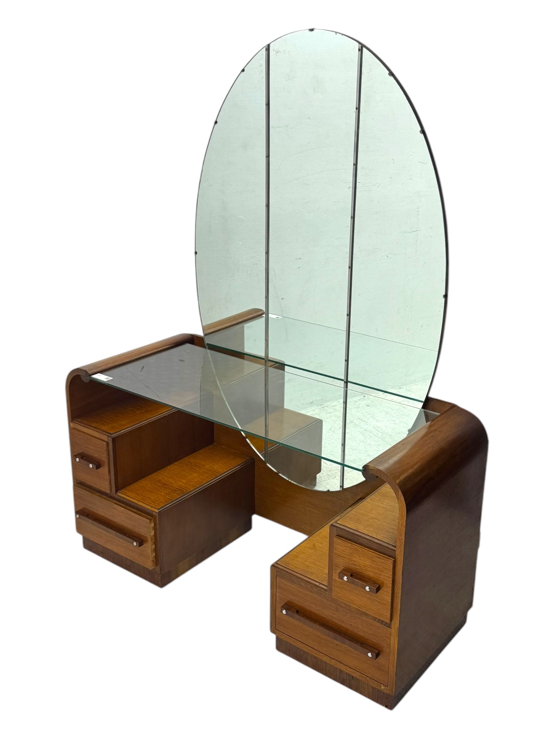 Early 20th century Art Deco walnut dressing table, featuring a large oval triptych mirror above a stepped base, fitted with four drawers and a central glass shelf, all raised on a plinth base