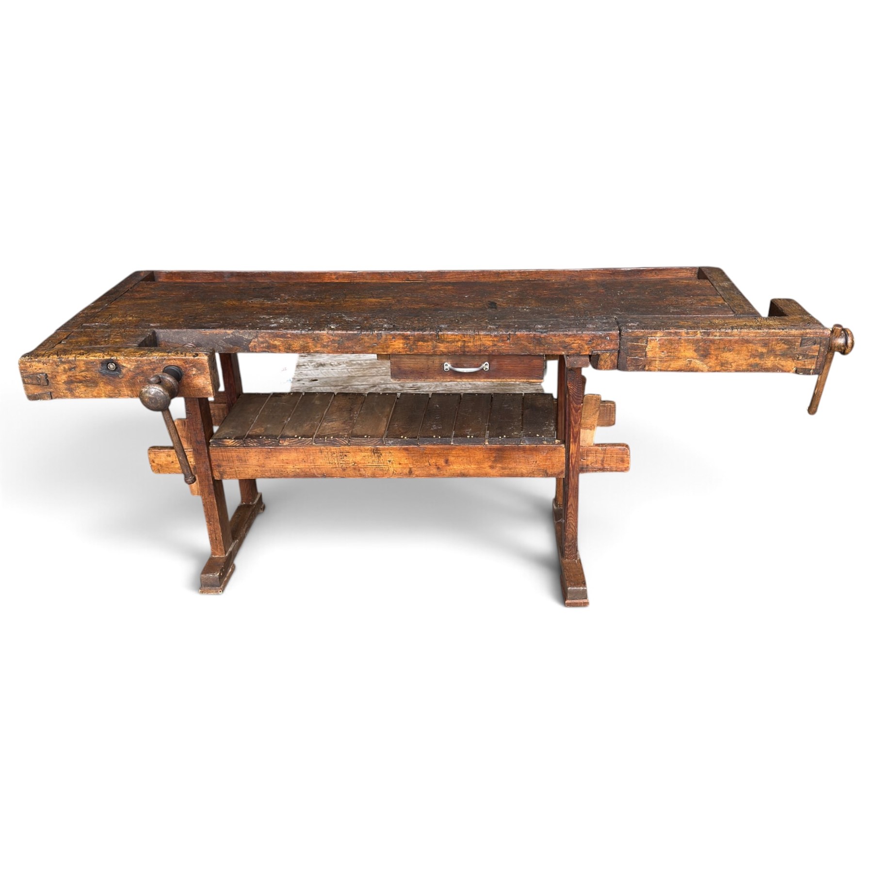 Large early 20th century rustic stained reclaimed pine workbench, the substantial plank top with recessed tool well and two homemade wooden screw vices, above a single frieze drawer and slatted undertier, raised on trestle end supports