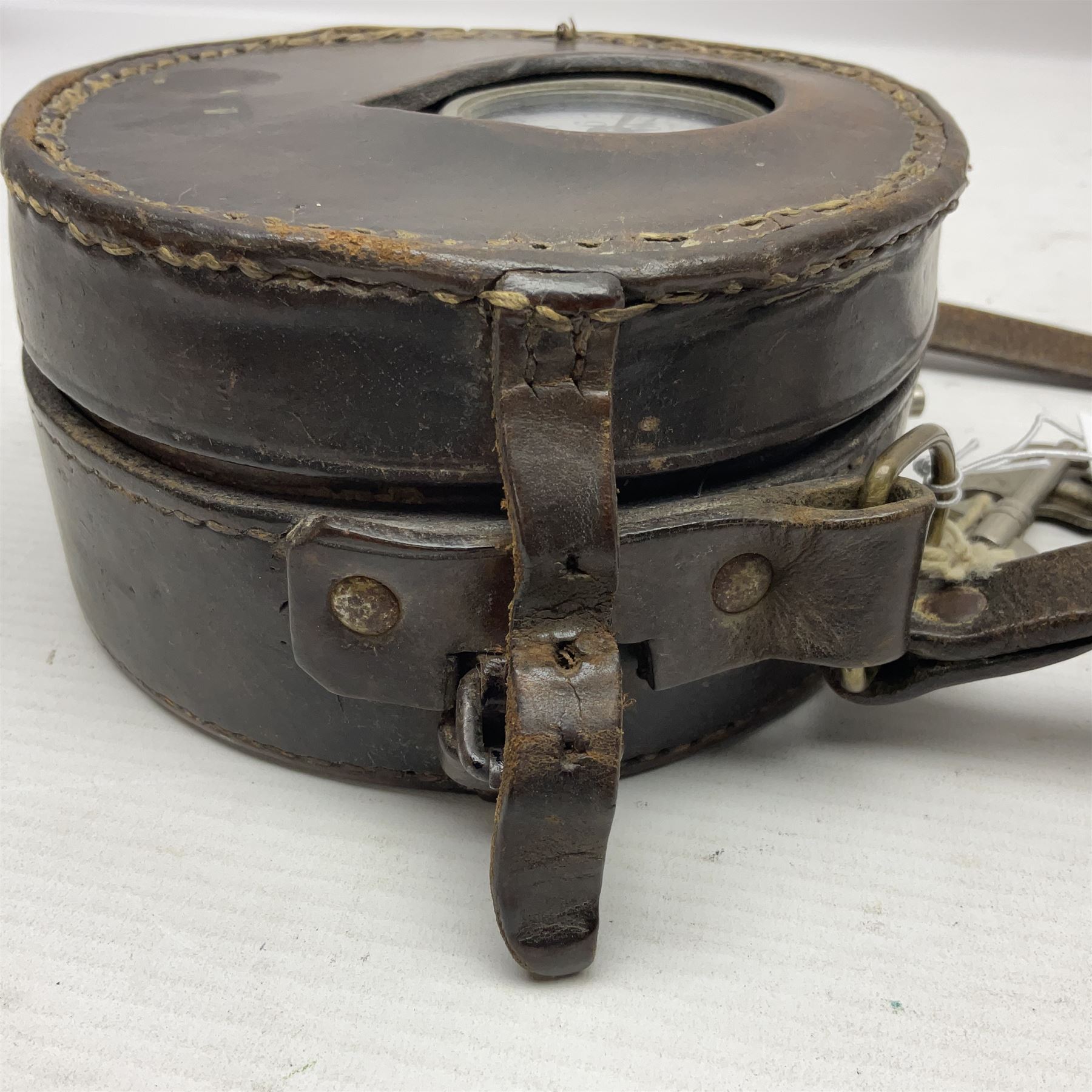 Metal cased drum shaped travelling clock with grey hammered finish, French clockwork movement and stitched leather outer case with shoulder strap; bears manuscript label 'Royal Armament Research and Development Establishment - serial no.09433' D13cm overall