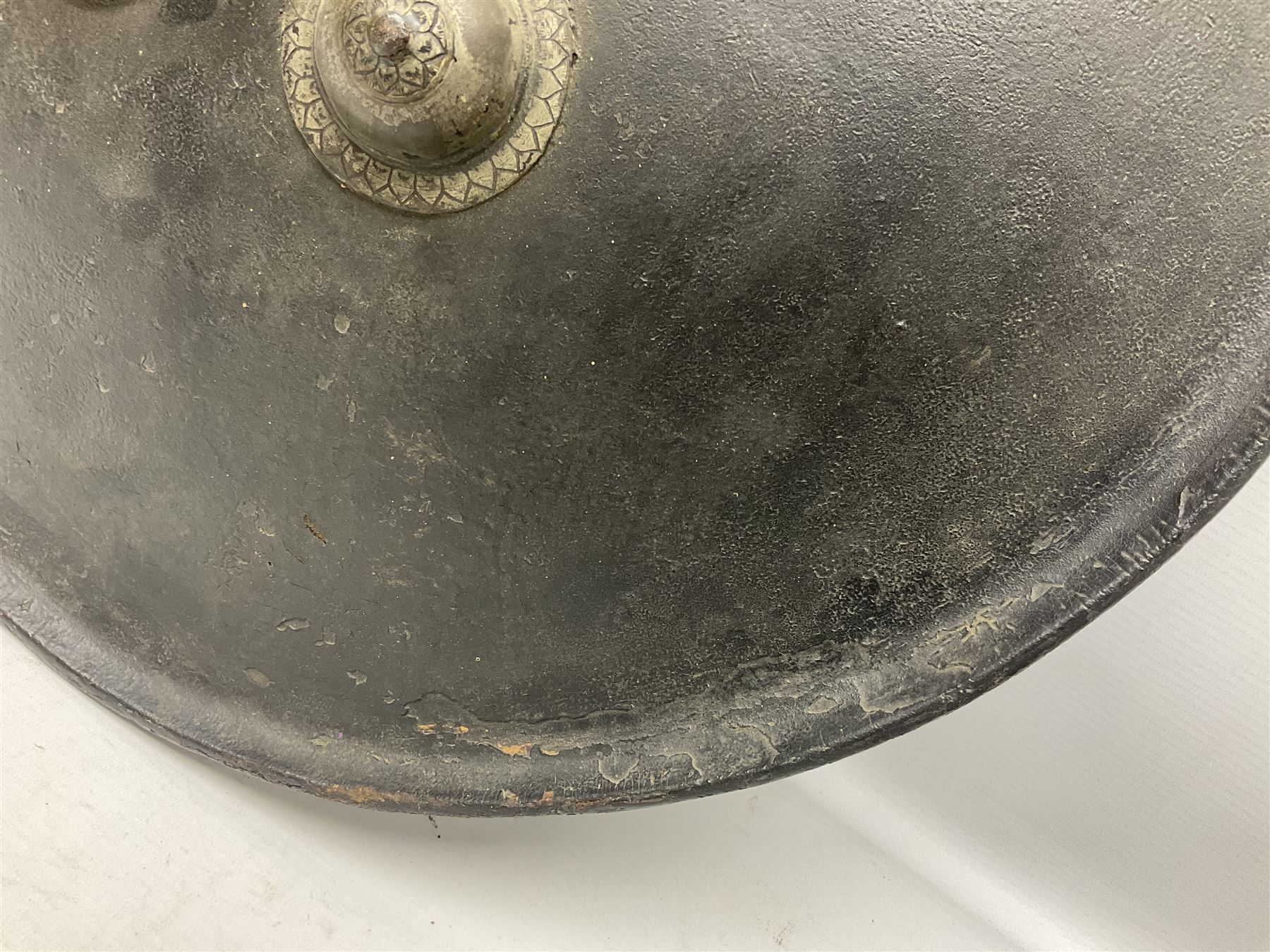 Indian black lacquered hide shield/dhal, of circular convex form with strongly outward-turned brim, fitted at its centre with four metal bosses, each of hemispherical form, with traces of silvered foliate decoration, the bosses corresponding on the inside with four iron rings for enarmes D49cm