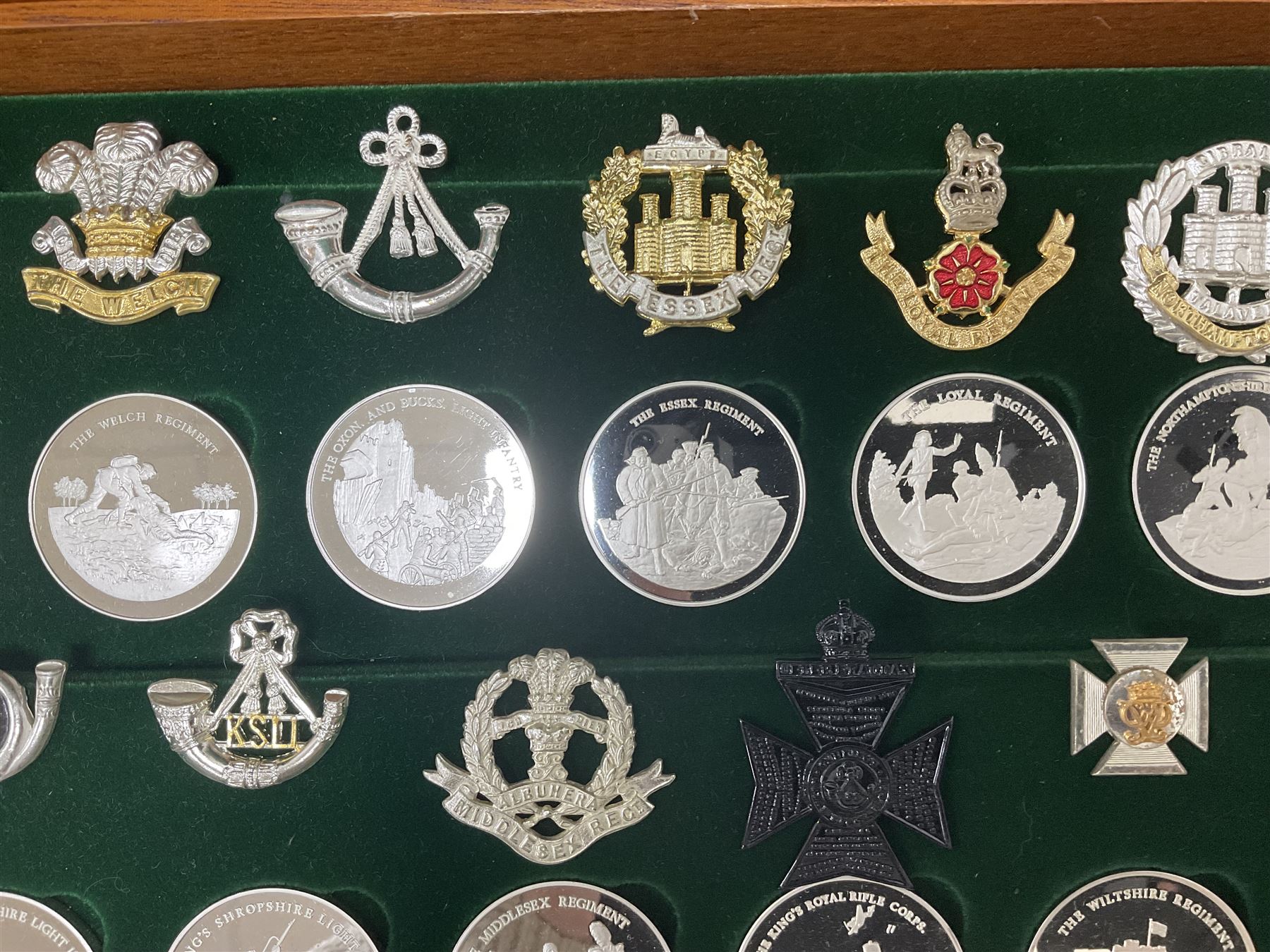 Great British Regiments, 1977, set of fifty two frosted silver medals by the Birmingham Mint, each bearing the name of a regiment with a depiction of an action on the obverse and further details on the reverse, all hallmarked Birmingham Mint, assay offices and dates; together with 52 base metal copy cap badges for each regiment, all housed and mounted on two trays and contained within a wooden presentation case, with brass plaque and fittings, lock and key, with a certificate of authenticity 