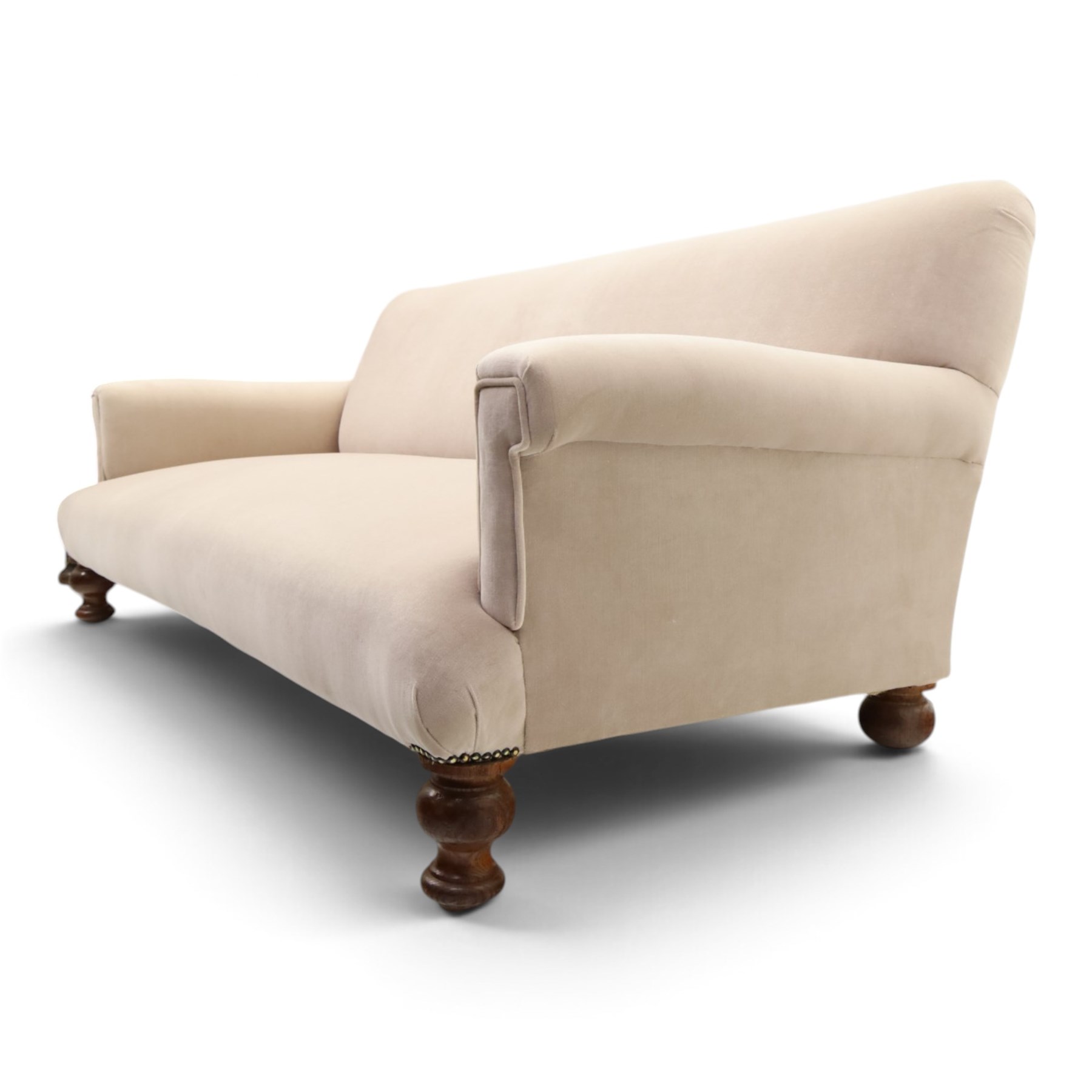 Late Victorian oak framed low three-seat settee, of traditional shape with low rolled sprung back over rolled arms and sprung seat, raised on front turned feet, upholstered in beige fabric