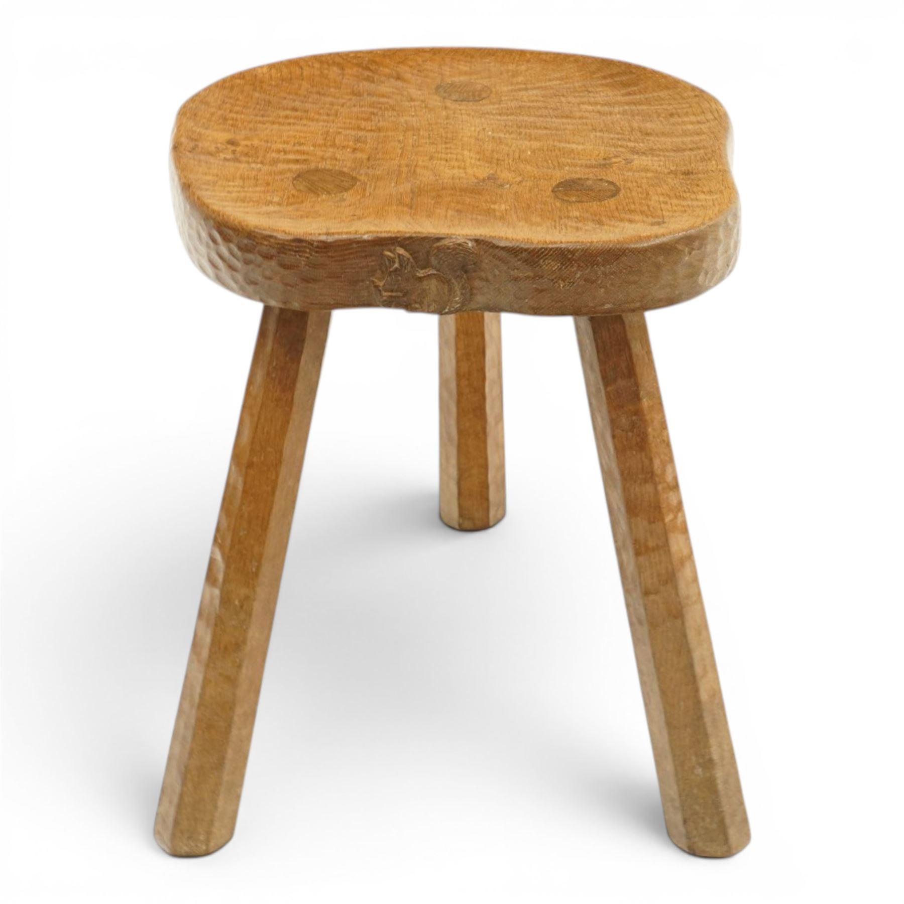 Squirrelman - rustic oak milking stool, adzed shaped top with exposed peg construction, on three tapering supports, with large carved squirrel signature, by Wilf Hutchinson, Husthwaite