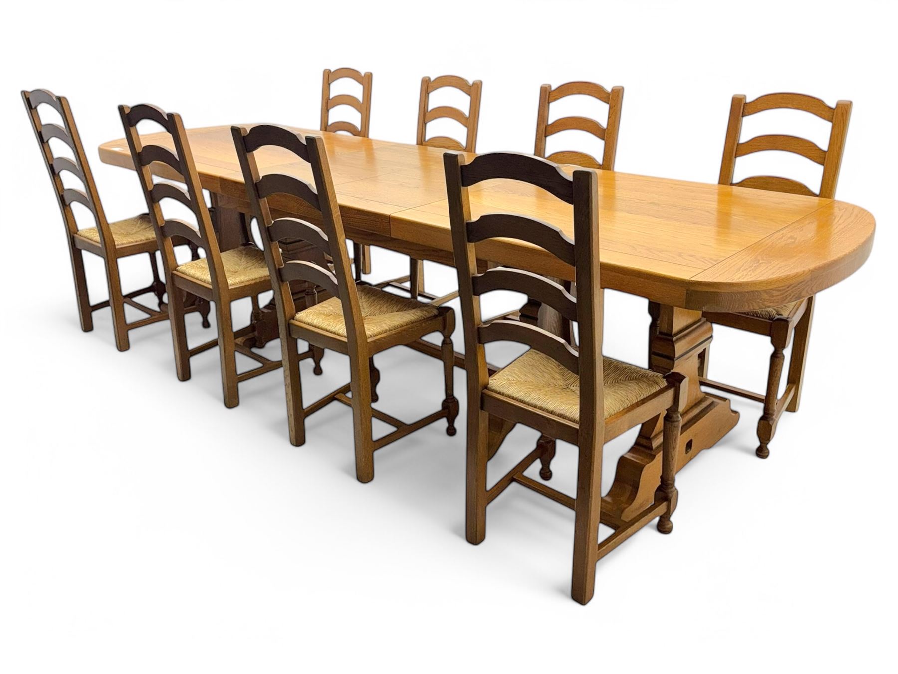 Oak extending dining table with elegant scrolled shaped double pedestal base and scrolled feet; together with a set of eight ladder back chairs with rush seats ((9) table closed 228x95x79cm chairs 106x38x44cm 