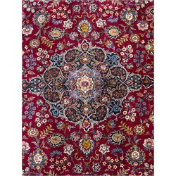 Central Persian Kashan hand-knotted carpet, madder red field with an intricate design of scrolling vines, palmettes, and rosettes with a central lobbed medallion with pendant motifs in shades of blue and ivory, and spandrels all within a blue-ground border of palmettes and flowerheads between multiple guard borders, 450cm x 335cm 