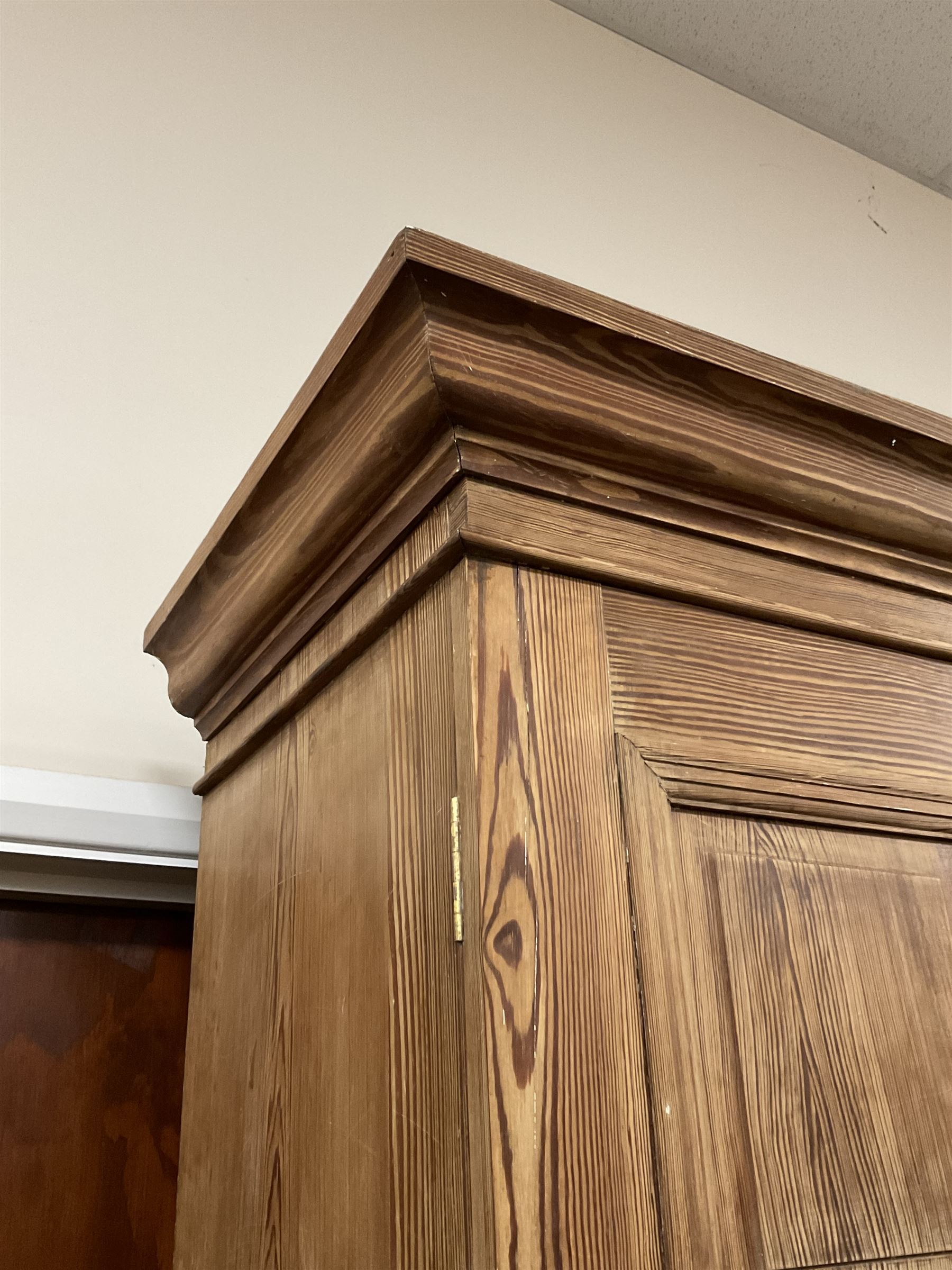 Victorian pitch pine double wardrobe, projecting moulded cornice over two panelled doors, the interior fitted with hanging rail and hooks, single drawer to base