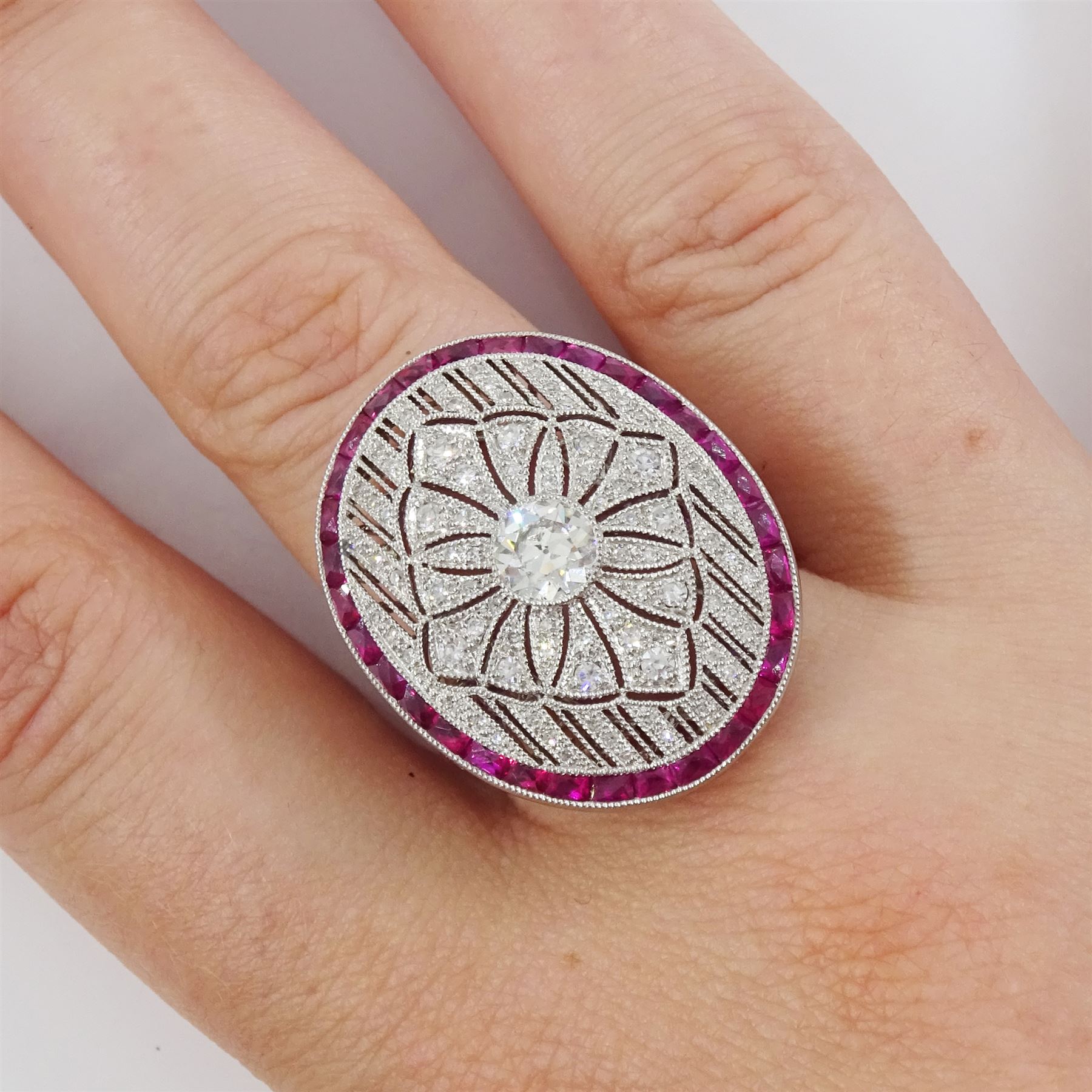 Platinum diamond and ruby oval cluster ring, principal transitional cut diamond of approx 0.55 carat, with milgrain set openwork diamond surround and calibre cut ruby border, with ruby and diamond shoulders