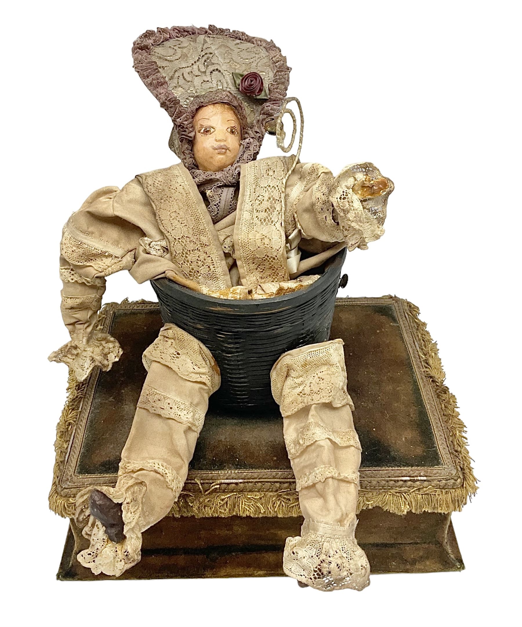 Modern reproduction automaton in the form of a baby doll in a basket clothed in Victorian style lace bloomers and frilled bonnet; clockwork action; on raised platform; with French paper label on base, 29cm wide,