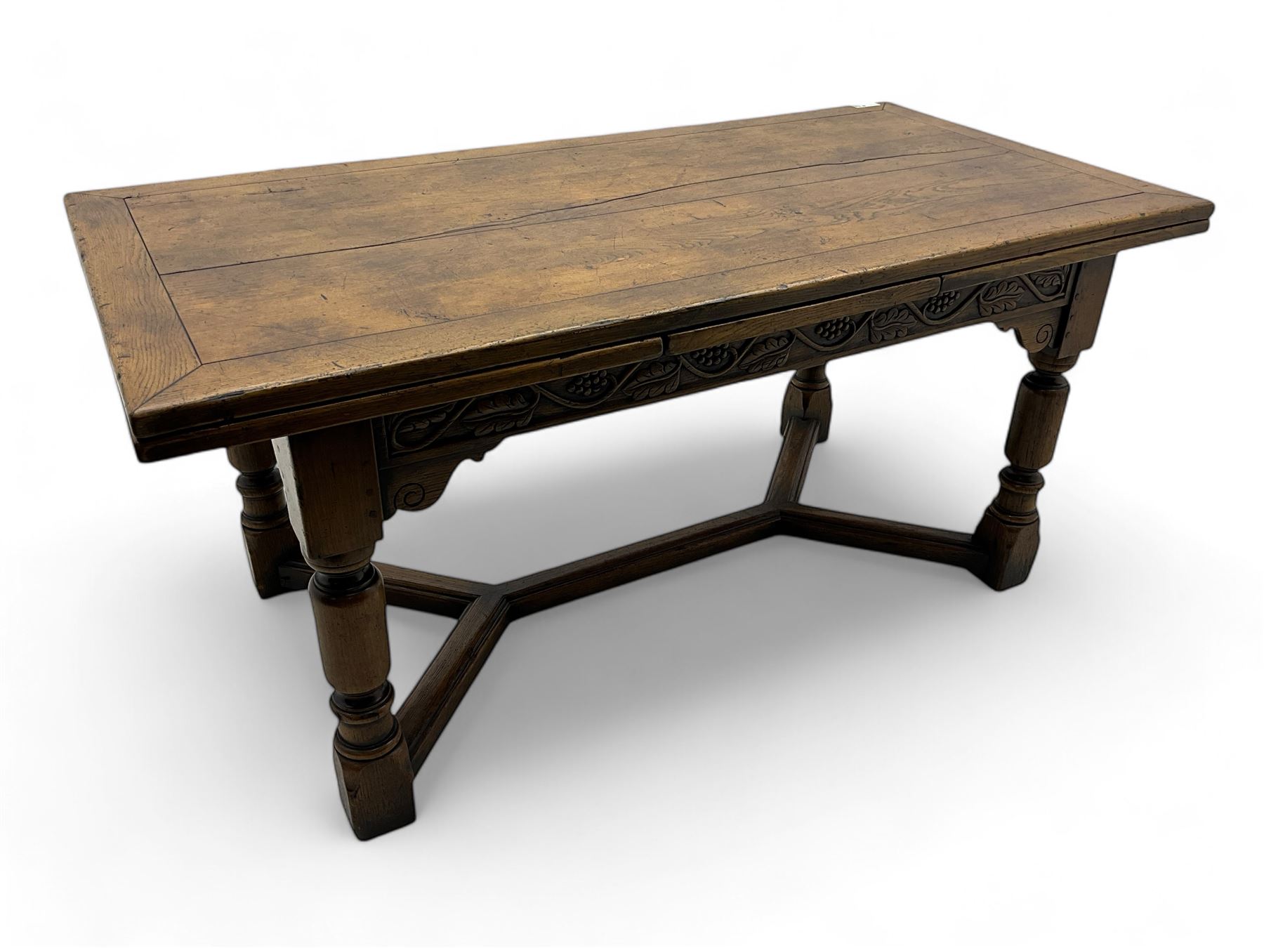 Early 20th century Jacobean design draw-leaf oak dining table, rectangular top with carved frieze depicting scrolling foliage and grape clusters, sliding extending leaves, raised on robust turned supports united by H-stretcher  