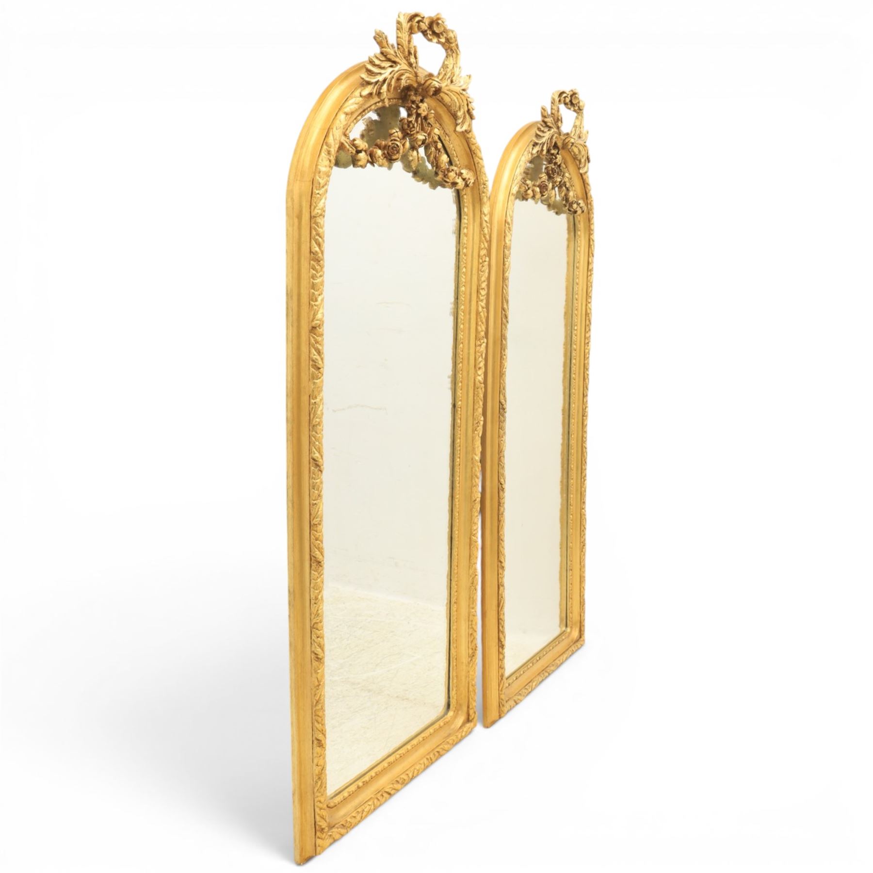 Louis XVI style giltwood pair of wall mirrors, arched frames with moulded borders, surmounted by ribbon tied floral crestings and trailing husk swags, enclosing bevelled mirror plates