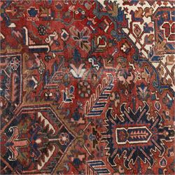 Persian Heriz carpet, red ground with large central geometric medallion, angular flowering branches and stylised foliate decoration, within a broad dark blue floral border and narrow guard stripes