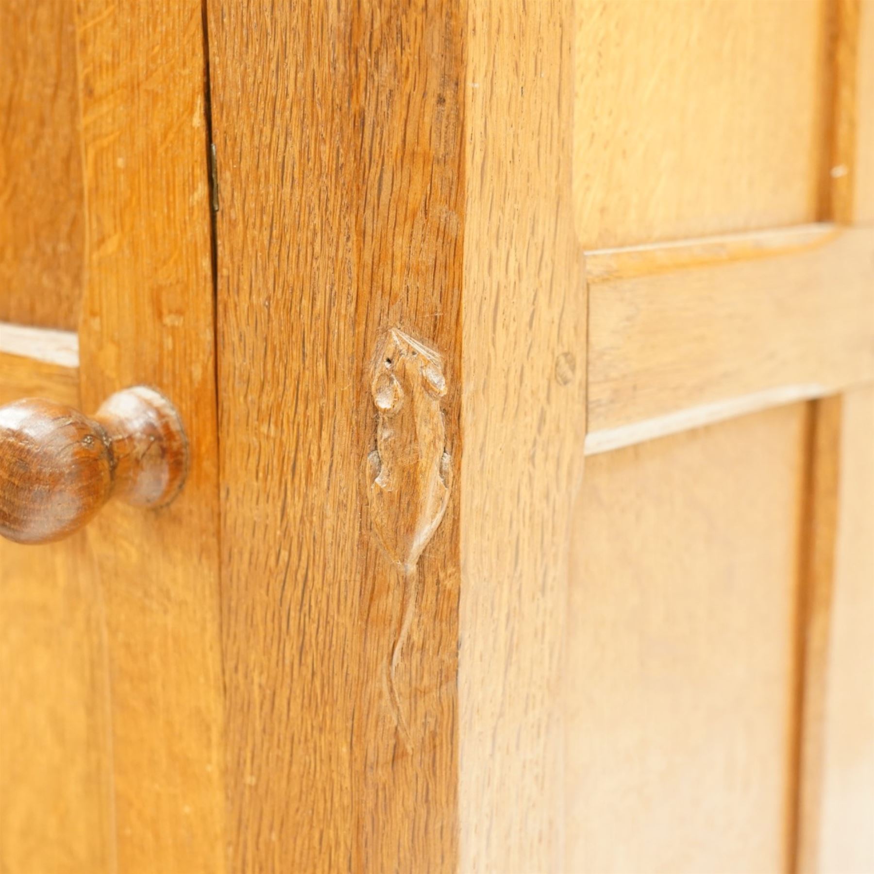 Mouseman - adzed and panelled oak bedside cupboard of small proportions, raised back over rectangular canted top, fitted with single panelled cupboard door with chamfered rails and turned knob handle, enclosing single shelf, raised on octagonal feet,  carved with mouse signature, by the workshop of Robert Thompson of Kilburn