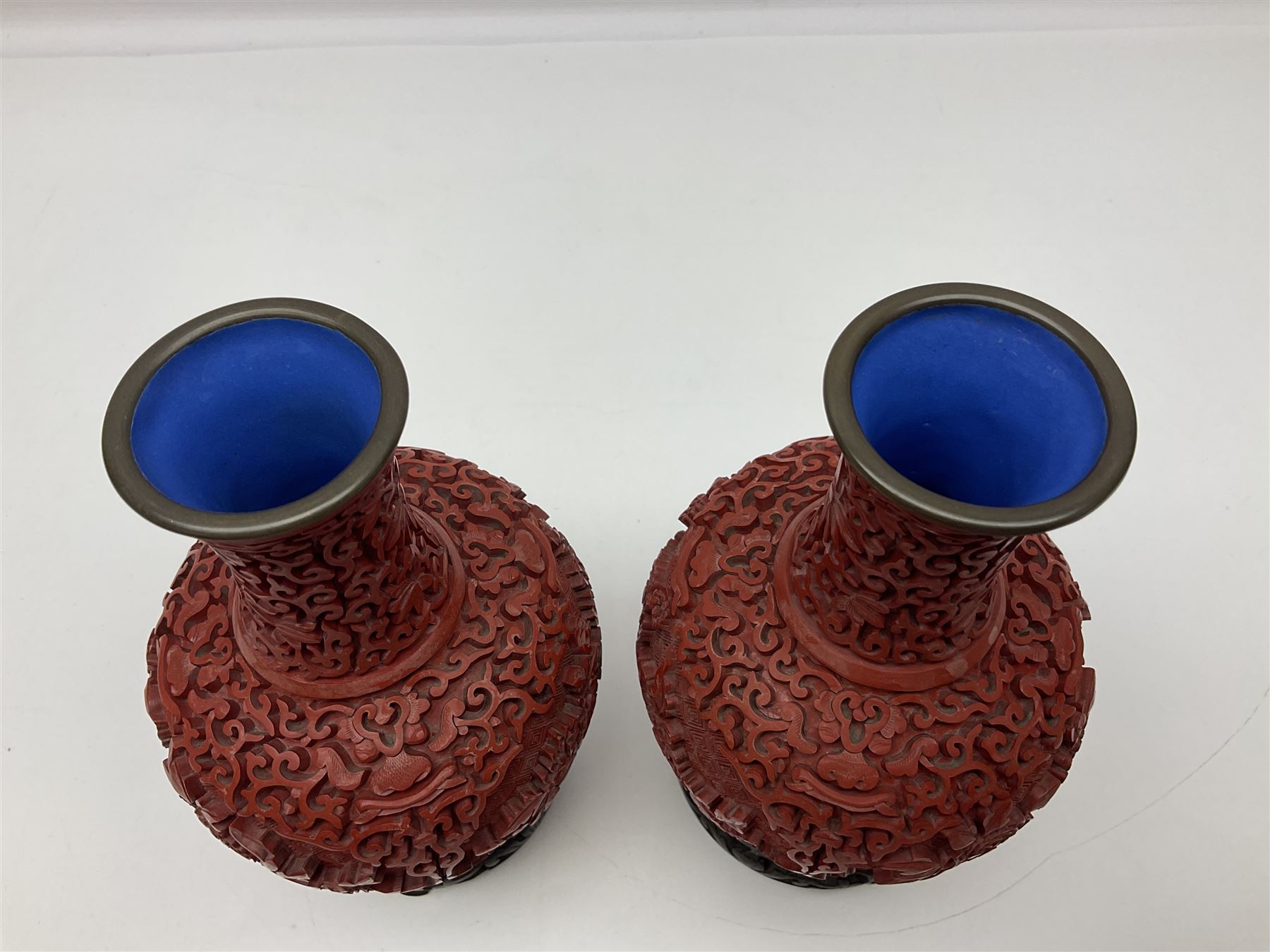Pair of Chinese cinnabar lacquer vases, each of bulbous baluster form, carved with peonies and foo dogs amongst scrolls, with blue enamel interior and upon wooden bases, H20cm
