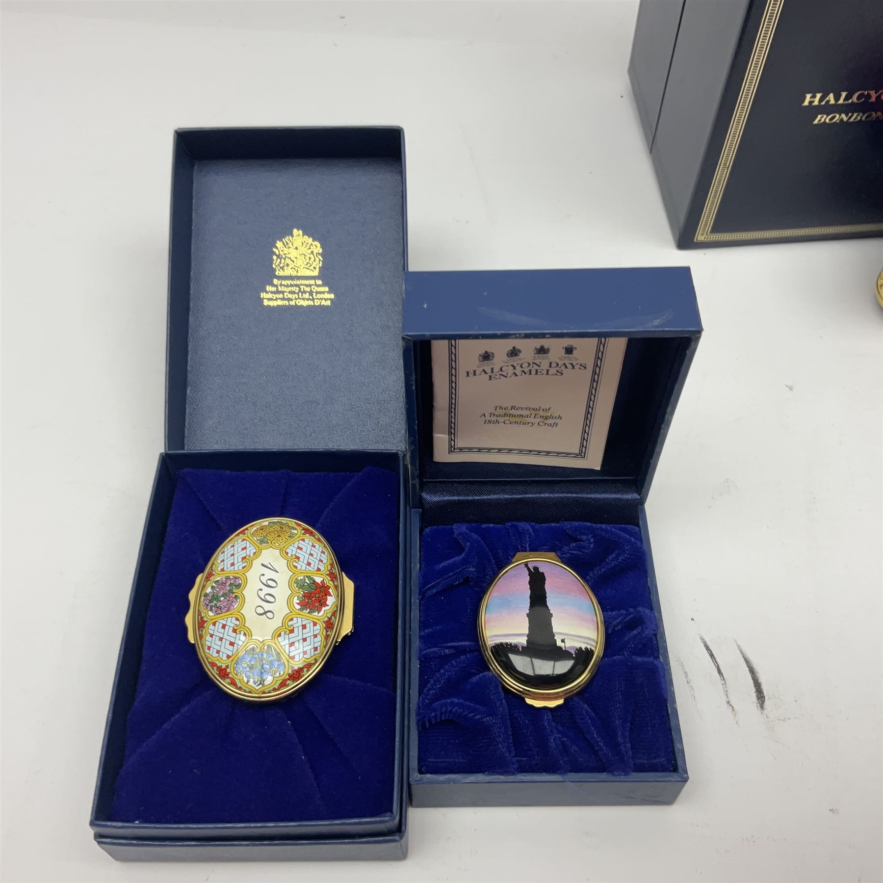 Halcyon Days bonbonniere, modelled as pink roses in a planter painted with a blue and white Japanese scene, together with five Halcyon Days enamel boxes, one a larger example depicting 'The Becket Casket' and four smaller boxes, including The 1993 Easter Egg, Happy Birthday and Statue of Liberty examples, all boxed, Becket Casket D8cm