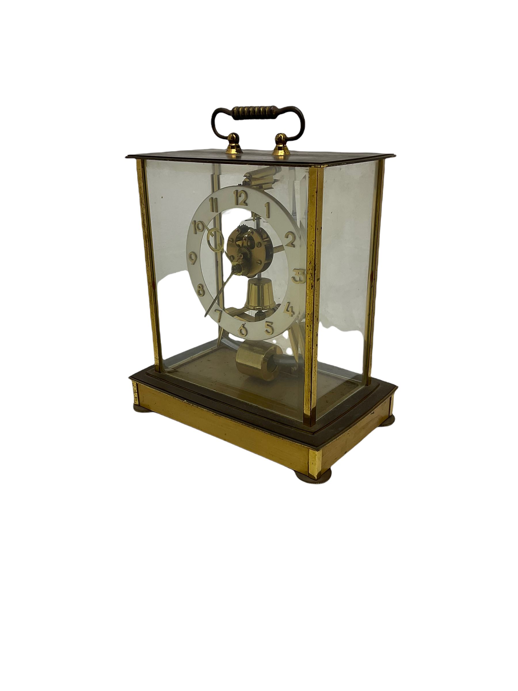 A  mid-20th century German Kieninger & Obergfell, “Kundo” battery operated 
mantle clock, rectangular case with four bevelled viewing panels and carrying handle, electrically operated solenoid pendulum powered via a battery housed in the base, skeleton movement with a visible escapement viewed through an open chapter ring with Arabic numerals and gilt baton hands.

