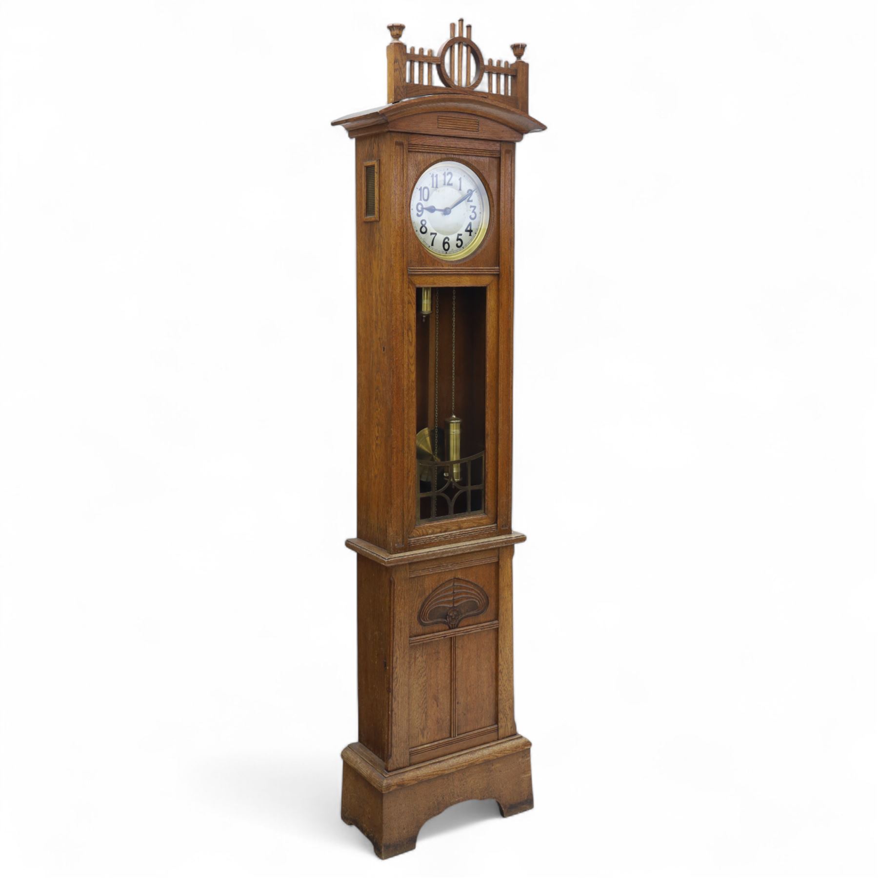 German-Art Deco 8-day longcase clock in an oak case, with a curved top and open fence work pediment, with reeded decoration and a fully glazed case door with a rectangular brass open work panel, on a tall rectangular plinth with a period  carved motif, circular slivered dial with Arabic numerals and spade hands, two train HAC (Hamburg and American Clock Company) weight driven movement, sounding the hours and half-hours on a coiled gong, with weights and pendulum.   