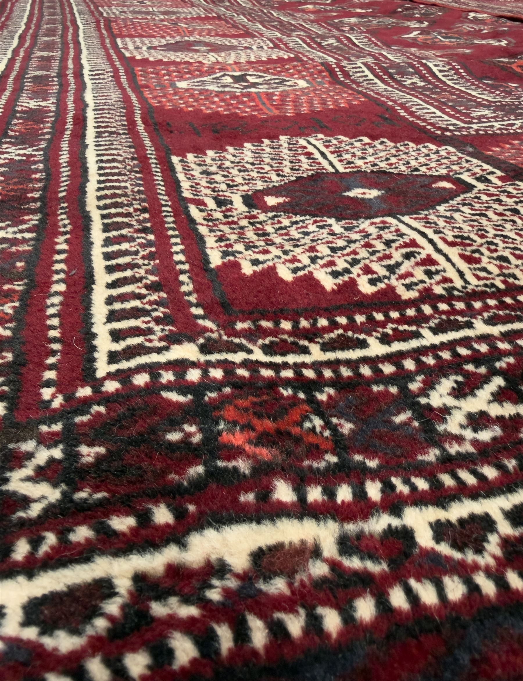 Northeastern Persian Yamut  hand-knotted carpet, the rich burgundy field with repeating rows of stepped gul motifs in cream and black, enclosed by multiple linear and geometric borders with hooked motifs and diamond medallions