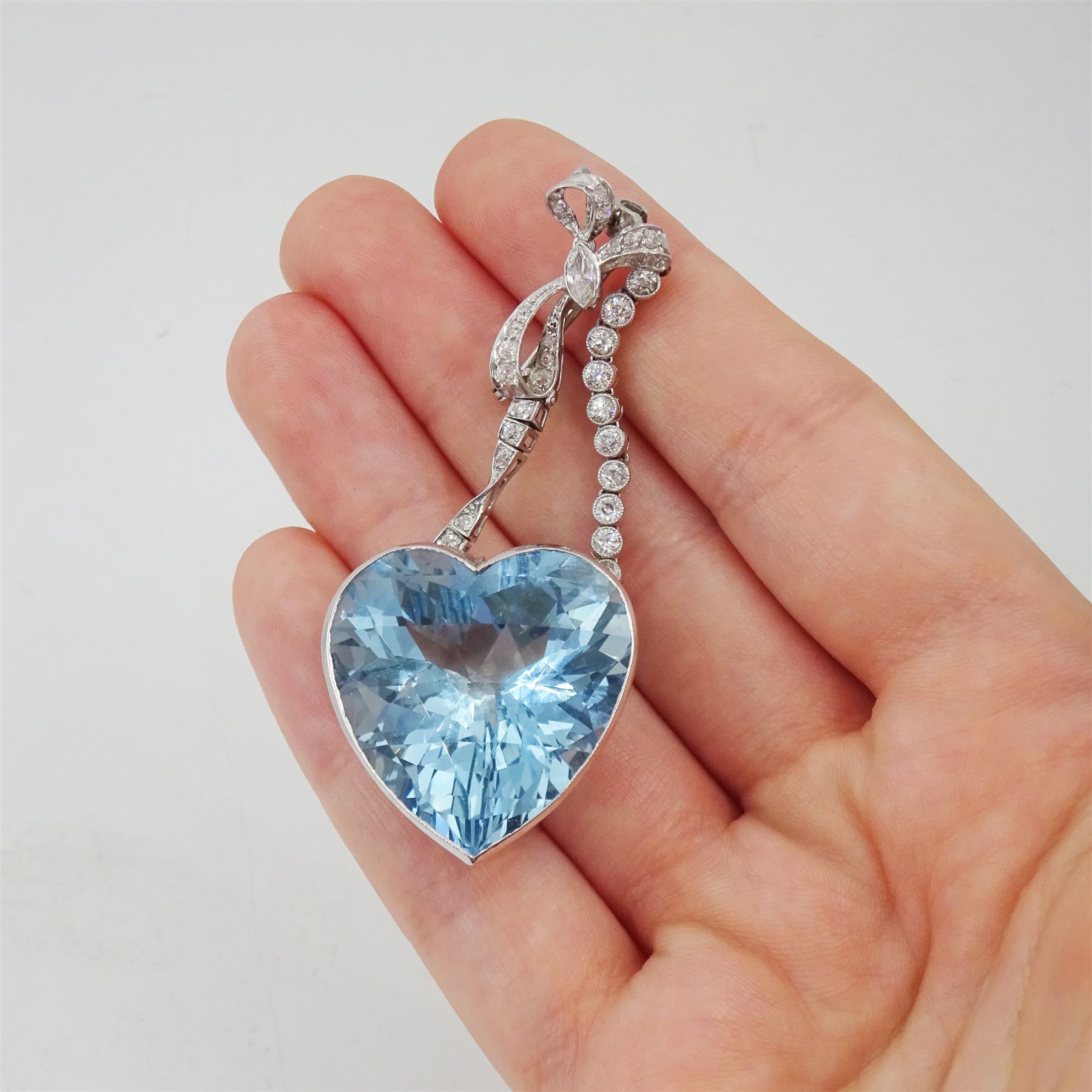 Platinum aquamarine and diamond pendant / brooch, the large faceted heart cut aquamarine, mounted within an openwork heart design gallery, suspending from a polished and milgrain set old cut diamond pendant, with bow design brooch top, set with further old cut diamonds and a single marquise cut diamond, in fitted velvet and silk lined box by Bloom & Sons, London, aquamarine approx 55.00 carat, total diamond weight approx 0.60 carat