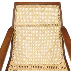 20th century teak framed plantation chair, plain cresting rail over cane back and seat, fitted with hinged extending leg rests, raised on turned front-supports united by ring-turned stretcher