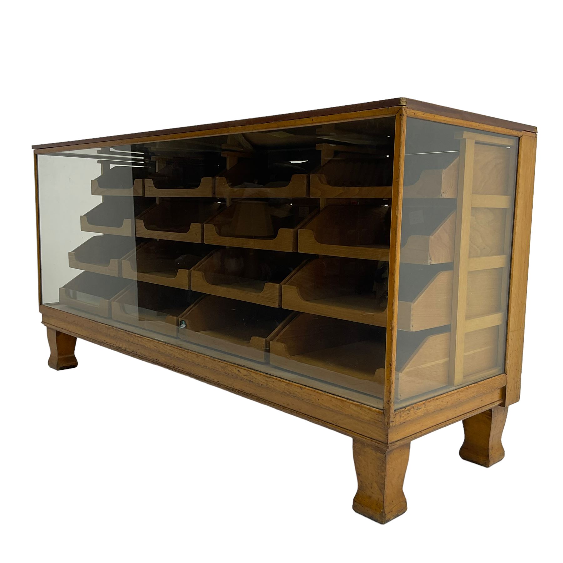 Early 20th century oak framed haberdashery shop counter, veneered top with glazed front and sides, fitted with sixteen graduating drawers with oak fronts and handles, raised on shaped supports