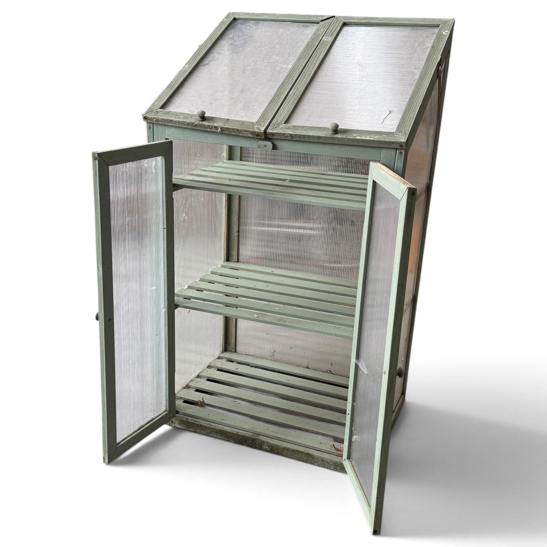 Three green-painted timber cold-frame greenhouses or growhouses, each with twin hinged sloping polycarbonate lids above a pair of panelled doors enclosing slatted shelves
