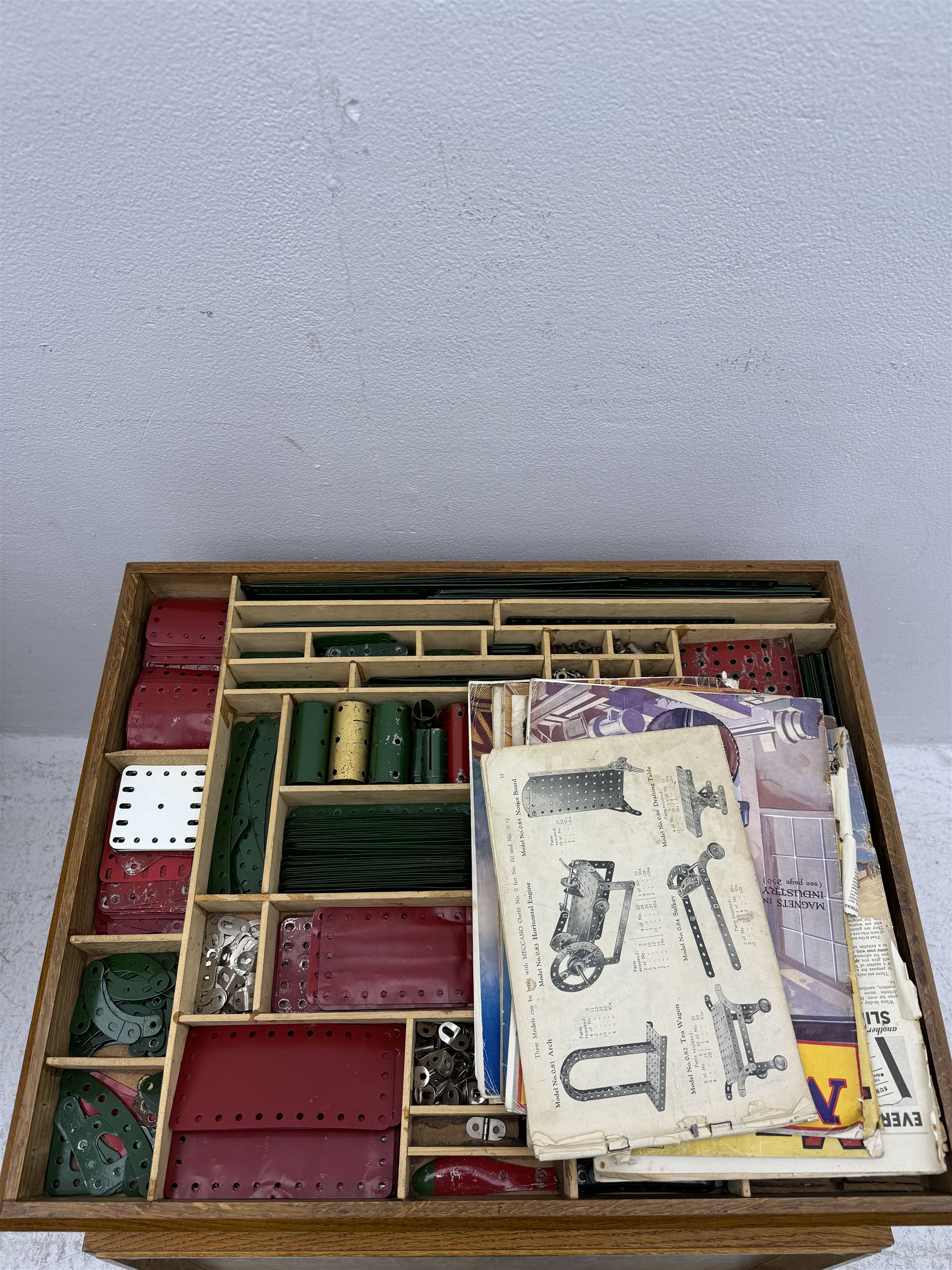 Large collection of Meccano, including perforated strips, wheels, cogs, nuts and bolts, various Meccano instruction manuals and magazines, all housed within a modified wooden box, with three tiered compartmentalised sections and upon four twist legs, box H60cm