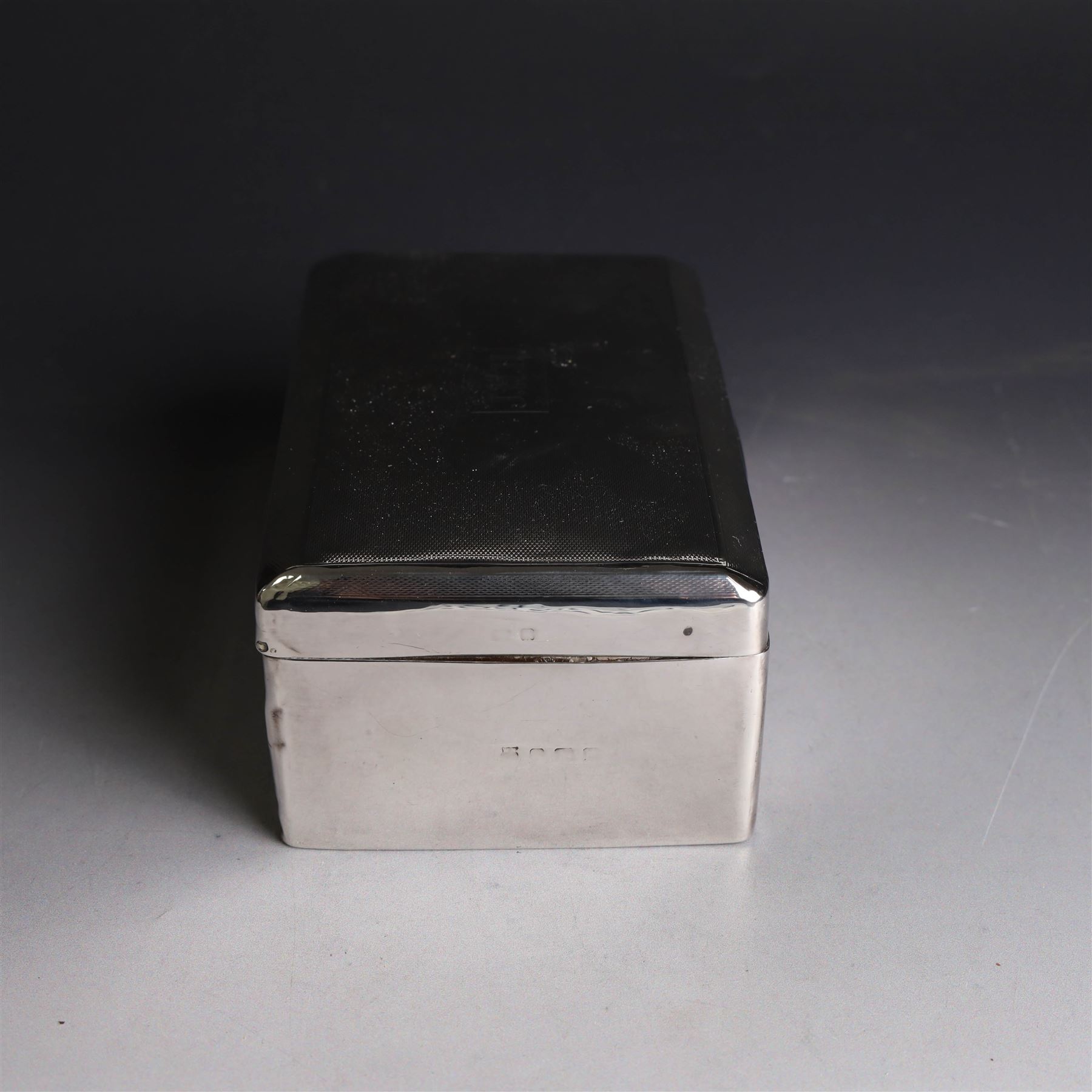Two silver cigarette boxes, comprising early 20th century plain rectangular example with compartmentalised softwood interior, hallmarked Birmingham 1914, maker's mark indistinct, and an early 20th century example with engine turned decoration and engraved initials to cover, hallmarks worn and indistinct, largest H4.5cm, W21cm