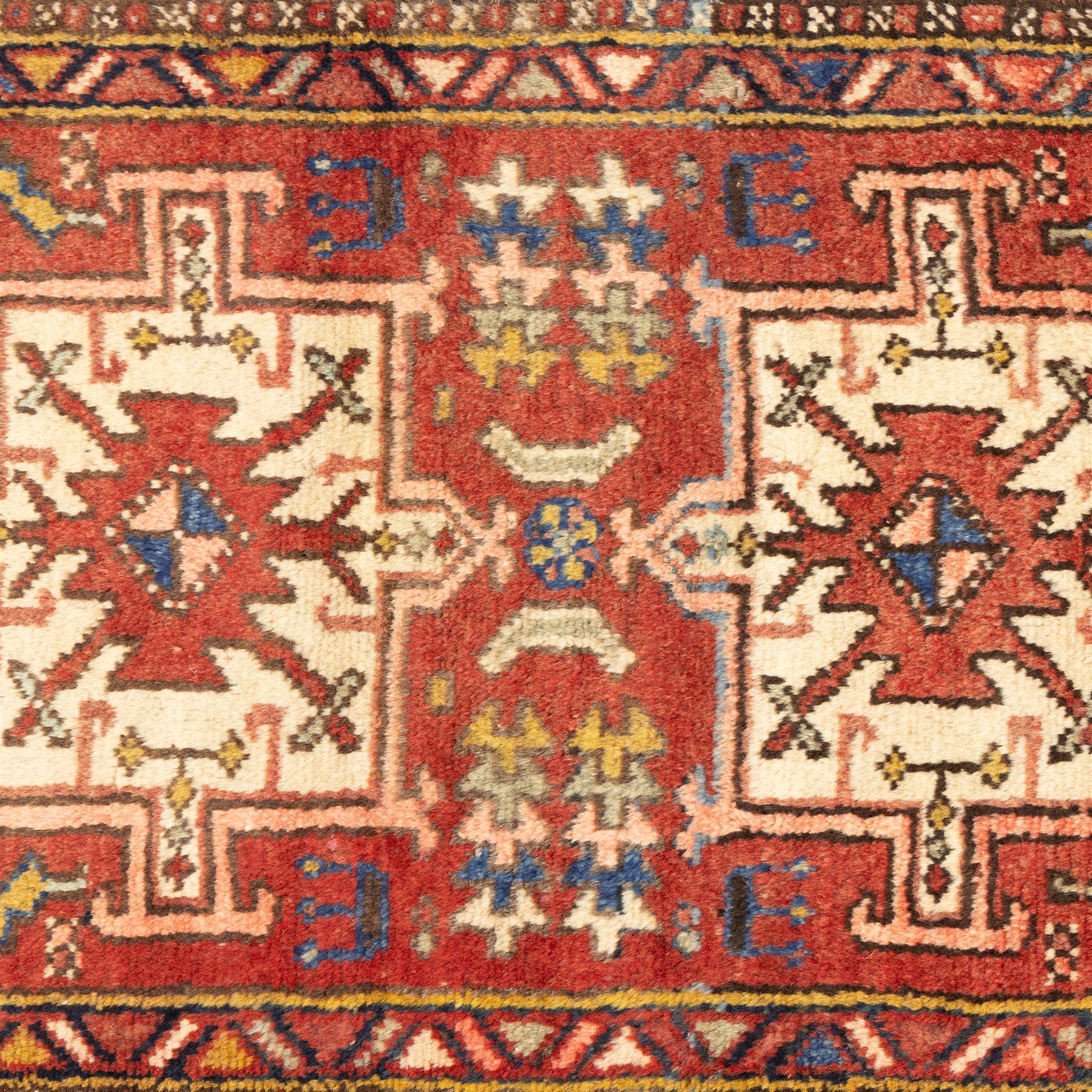 North west Persian Heriz runner, madder red field with a single column of alternating hooked and stepped lozenge medallions in ivory, blue, and terracotta, scattered with small cruciform and geometric motifs within a brick red border, angular motifs between narrow guard stripes 