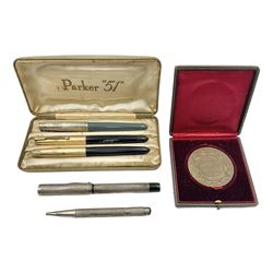 Three parker fountain pens, one example with 14ct gold plated cap and personal engraving, in Parker 51 box, together with a silver Sampson Mordan Everpoint propelling pencil with personal engraving and a silver cased fountain pen with 14ct gold nib and a souvenir bronze Dollfus-Mieg medallion, awarded to John G Sedorski, in fitted case 