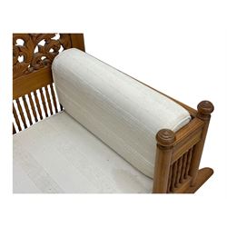 Early 20th century carved teak Howdah elephant chair, with pierced floral and foliate carved backrest, spindle gallery arm supports, cream upholstered cushions, splayed legs on a curved reeded base 