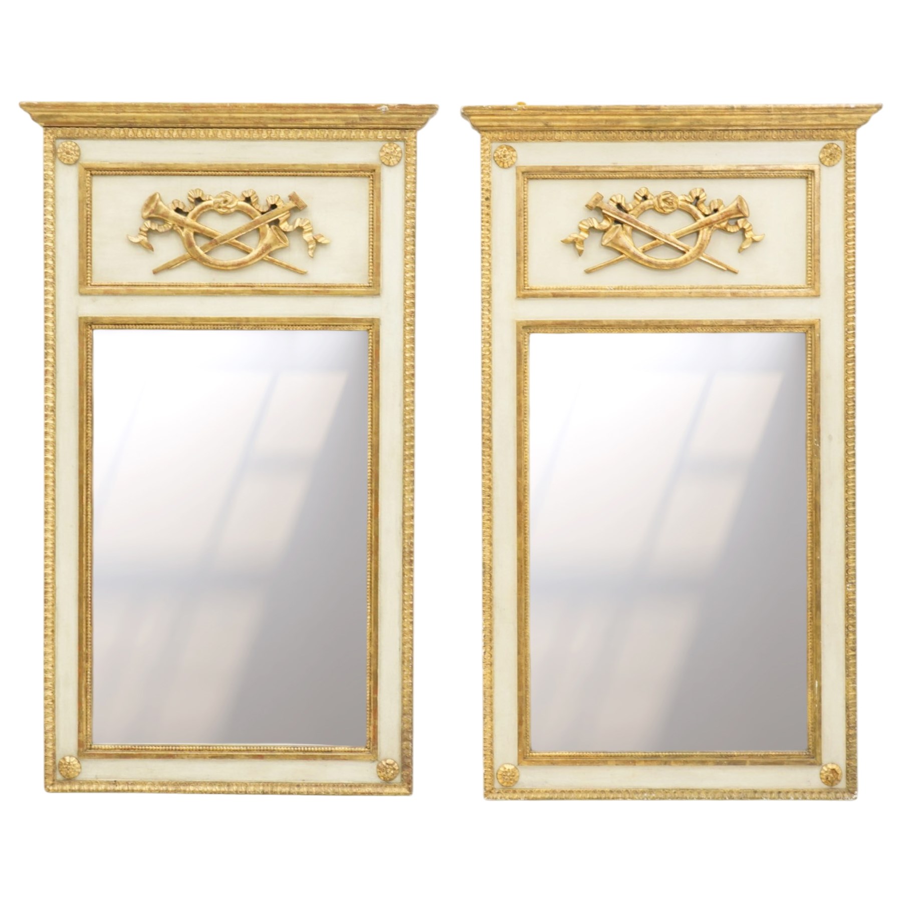 Neoclassical design pair of cream painted and gilt pier mirrors, projecting moulded cornices above frieze panels decorated with ribbon-tied musical trophies, rectangular plates within beaded slips, the outer frames with repeating leaf borders and flowerhead roundels