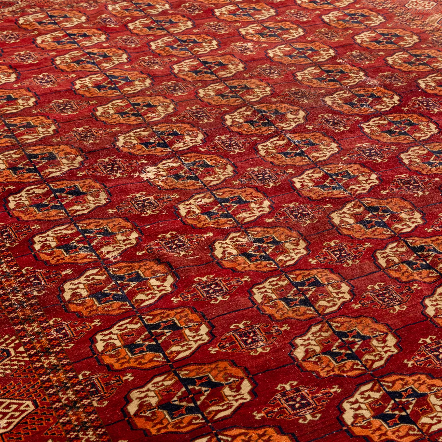 Vintage Bokhara hand-knotted rug, madder field woven in rows of octagonal Tekke guls arranged in vertical columns, each enclosing angular cruciform devices and tribal motifs, divided by narrow indigo lines, within multiple geometric borders incorporating stepped lozenges and latch hook devices, with cotton fringe ends 
