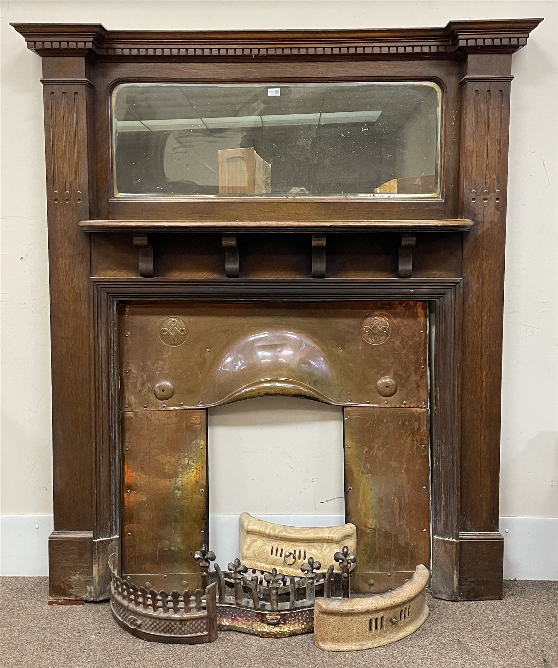 Late 19th/early 20th century fireplace, oak surround with projecting dentil cornice over bevelled mirror and shelf, with copper inset decorated with Heraldic knot motifs and rivets, together with various fire accessories 