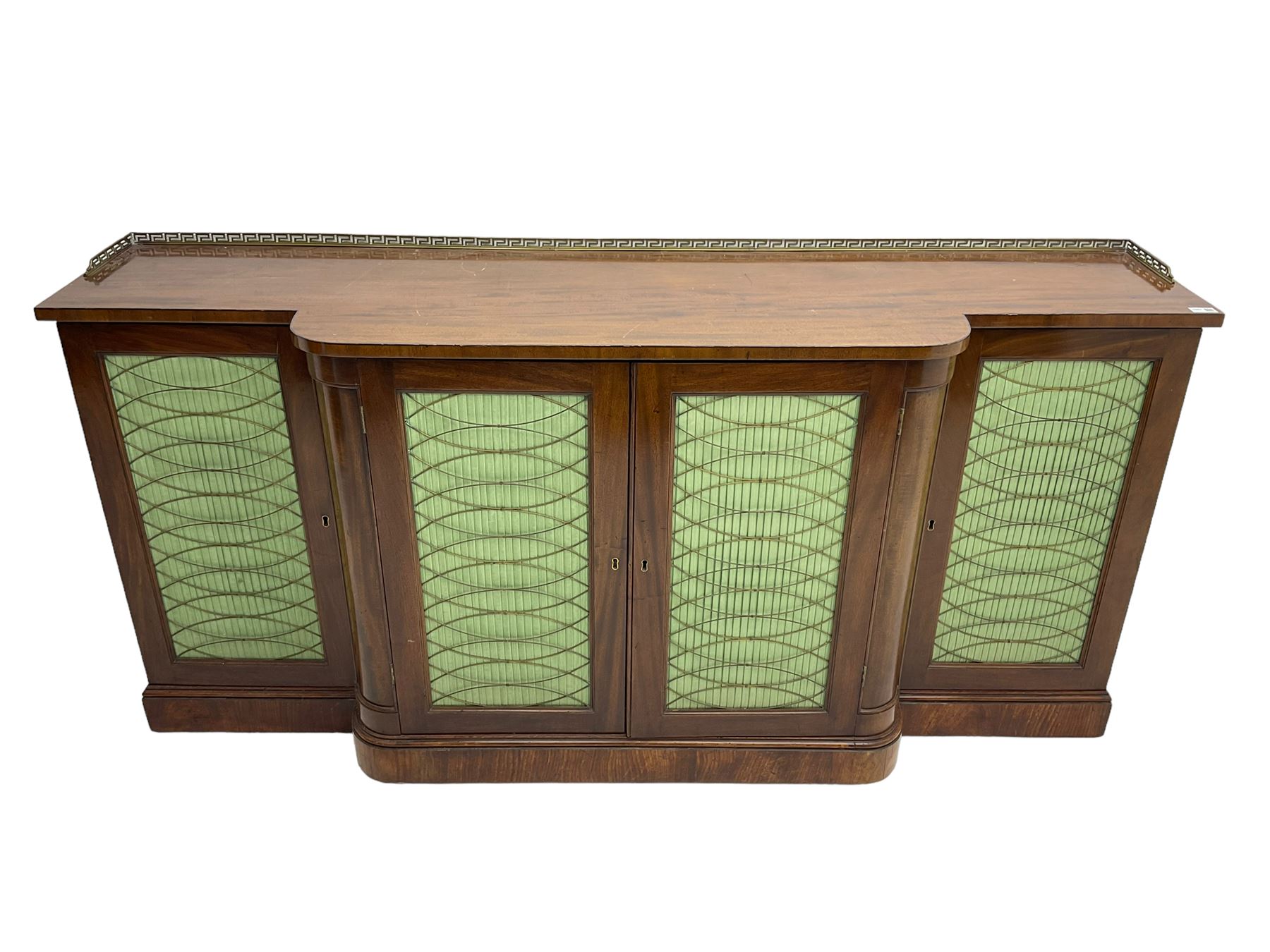 19th century mahogany break-front sideboard, raised brass gallery back with Greek key design, fitted with four cupboard doors, their pleated green fabric overlain with gilt metal grilles, lower moulded edge over plinth base