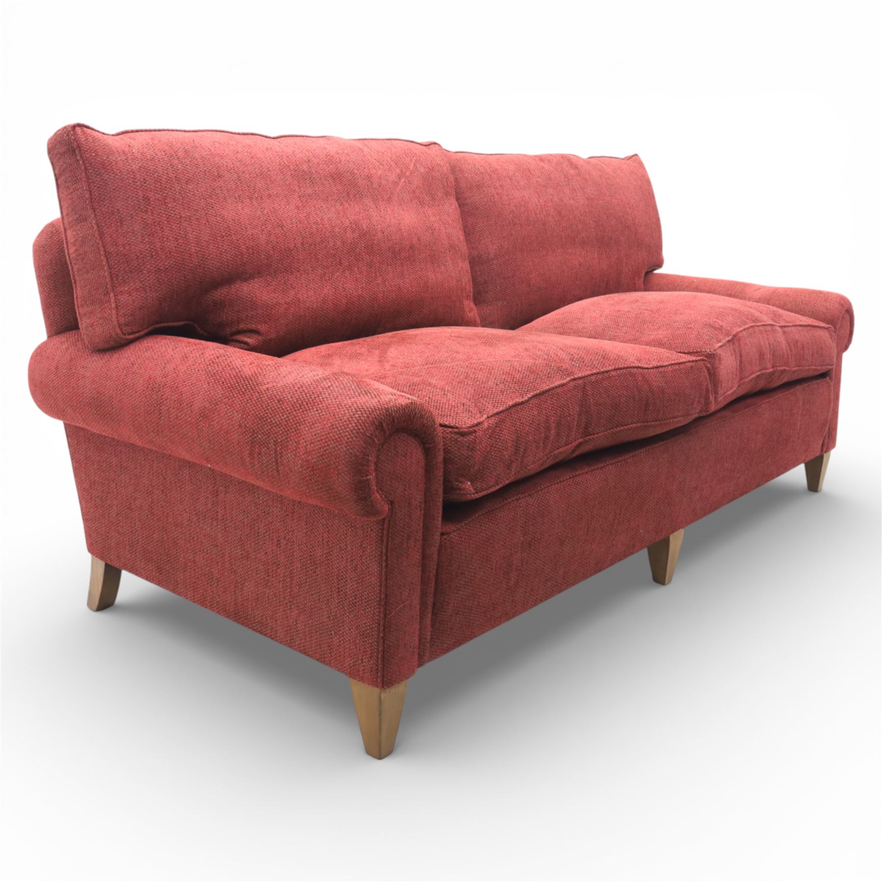 Late 20th century three seat sofa upholstered in red fabric, with gently rounded scroll arms, loose seat and back cushions, raised on tapered wooden legs