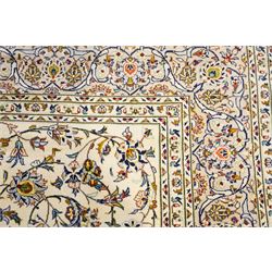 Central Persian Kashan hand-knotted carpet, ivory field decorated with an all-over scrolling floral vine design incorporating stylized palmettes, rosettes, and foliate sprays in the Shah-Abassi style enclosed by a series of floral vine borders and multiple narrow guard stripes, cotton fringe ends 