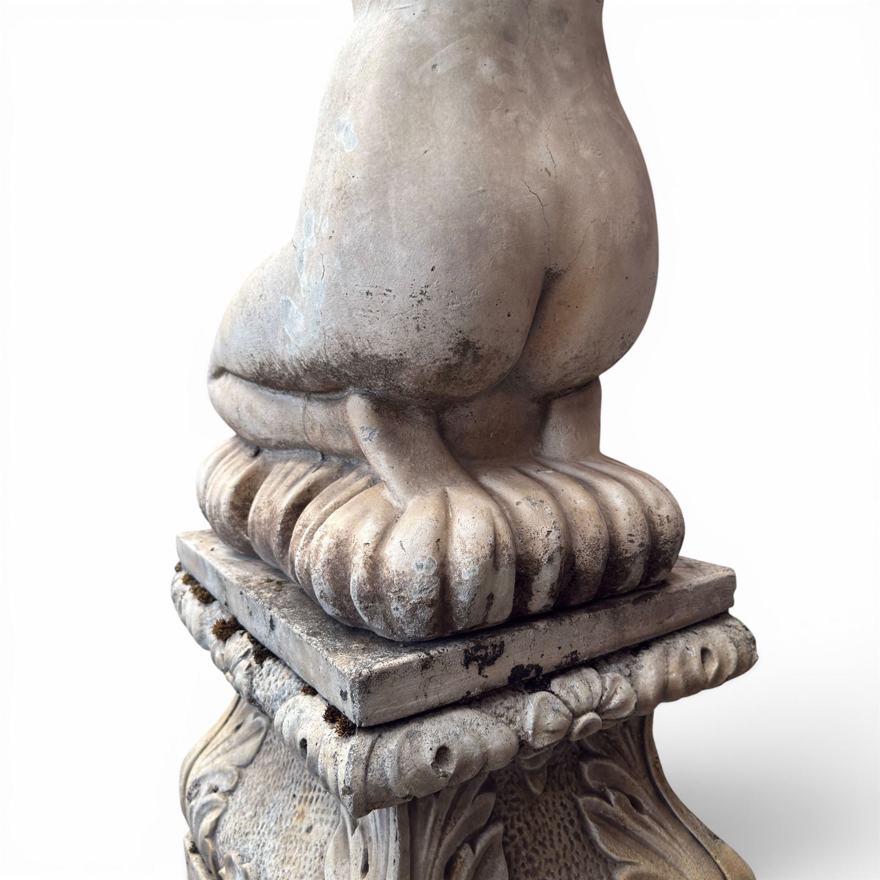 20th century composite stone garden figure, modelled as a kneeling nude female with arms raised behind her head, mounted on an integral cushion, the squared ogee pedestal moulded with acanthus leaves and flower heads, in a white painted and weathered finish
