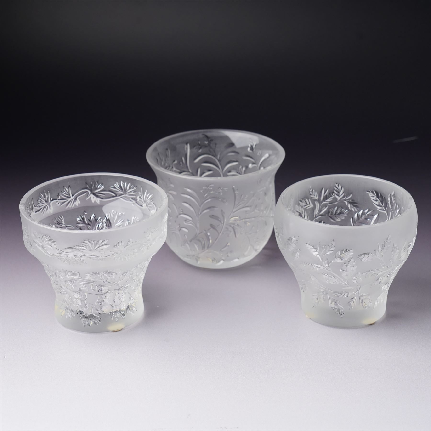 Three Lalique frosted glass tea light holders, decorated with the coriander and basil patterns, and another with trailing leaves, marked Lalique France to base, H7.5cm