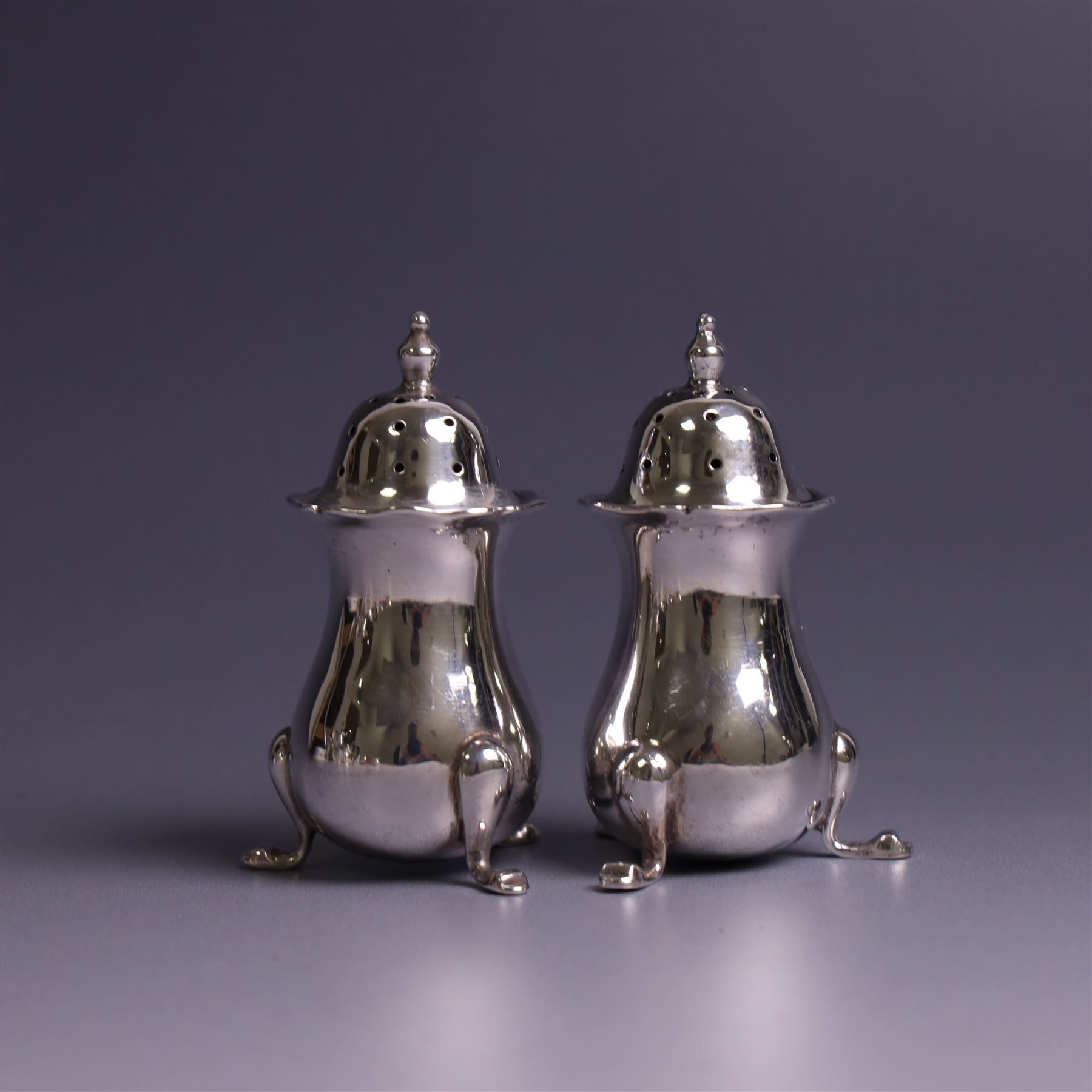 Early 20th Century four piece silver cruet set, comprising a pair of pepper shakers and a pair of open salts, each of circular form with shaped rims and upon three pad feet, hallmarked Walker & Hall, Sheffield 1912, the open salts with two silver plated salt spoons and blue glass liners 