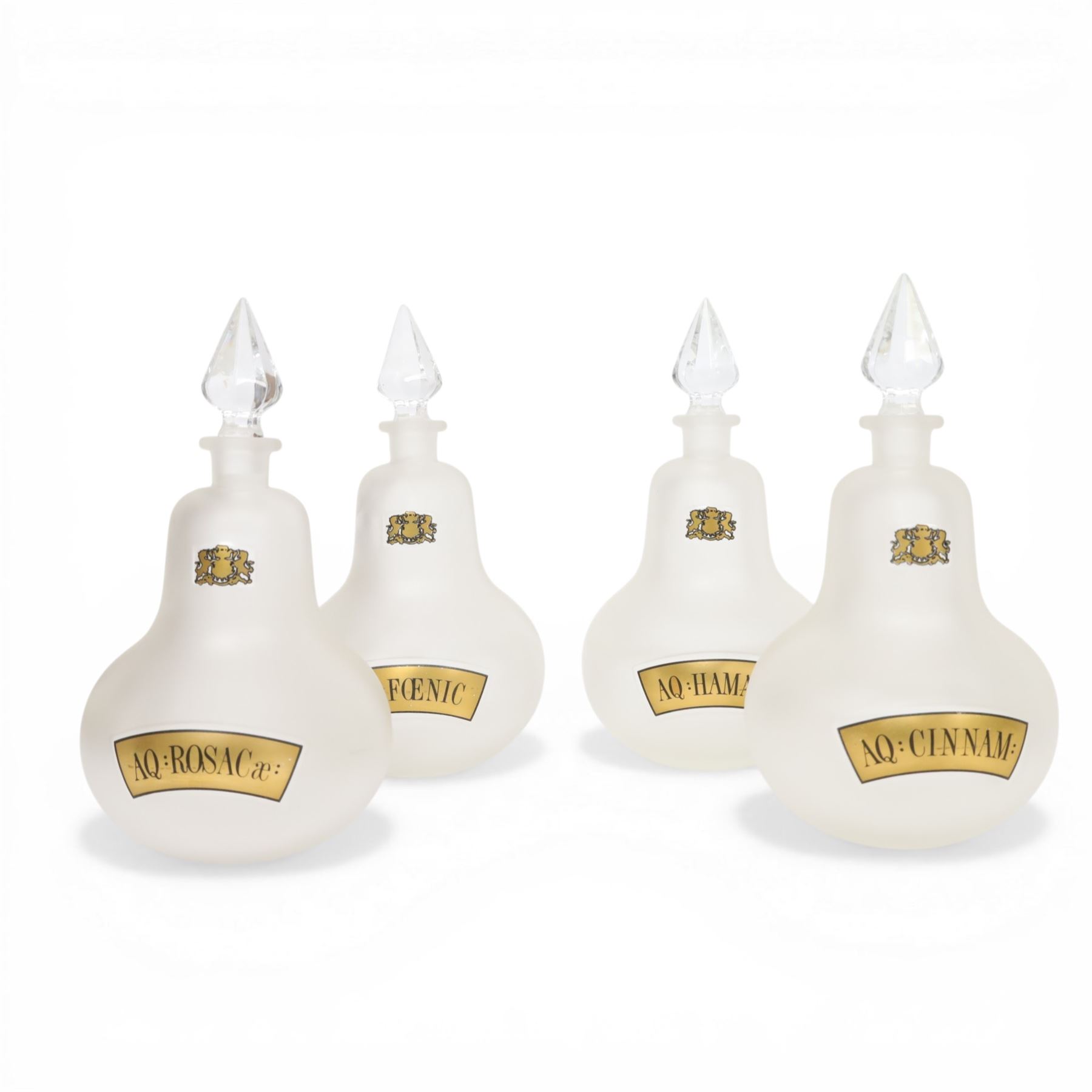 Set of four 20th century Royal Pharmaceutical Society white frosted glass bottles, of bellied form with clear cut glass spire stopper, each body bearing gilt label in Latin: AQ:CINNAM:, AQ:FOENIC:, AQ:HAMAM:, and AQ:ROSACae:, and gilt Royal Pharmaceutical Society crest to neck, H25cm

Provenance: From the collection of the family of Peter Green, a practising pharmacist whose career spanned the mid to late 20th century. During his professional life he managed pharmacies in Yeovil, Somerset, and later Selles Chemist in Filey, North Yorkshire, before purchasing and running his own business, Peter Green Pharmacy, located in the Market Place, Malton. The bottles were displayed as part of the traditional shop fittings in both the Filey and Malton pharmacies and were retained as part of his collection.