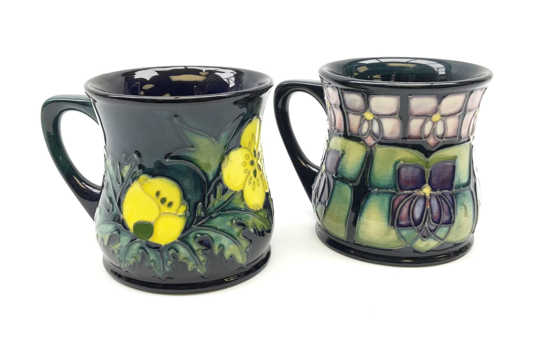 Two Moorcroft mugs of waisted form, the first example decorated in the  Violet pattern designed by Sally Tuffin, the second example decorated in  the Buttercup pattern designed by Sally Tuffin, each wit -