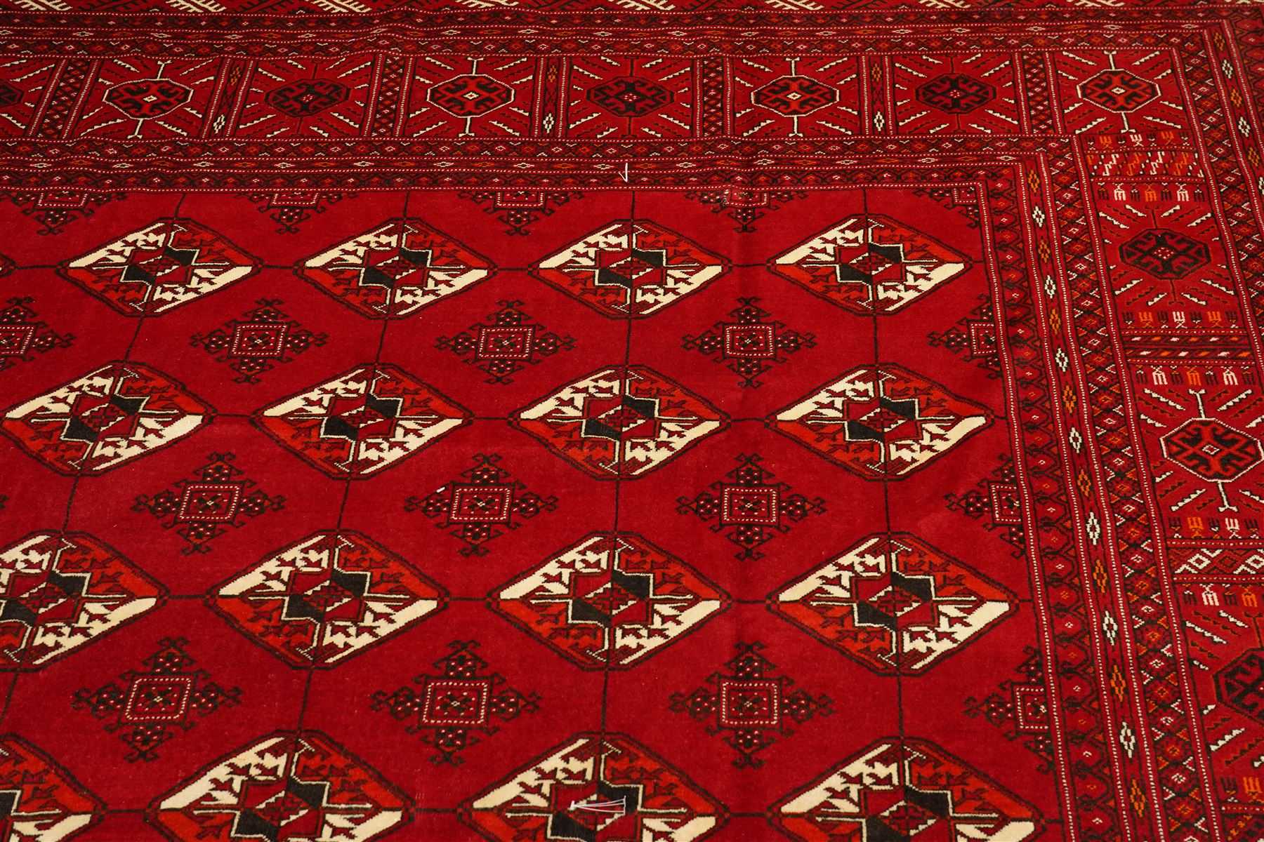Turkmen hand-knotted carpet, deep crimson ground field, with an all-over lattice of repeating diamond guls, each enclosing angular cruiform motifs, and stylized tribal devices, interspersed with smaller geometric ornaments, main border decorated with repeating geometric motifs and stylized tribal elements, flanked by narrow guard stripes, with cotton fringe ends 