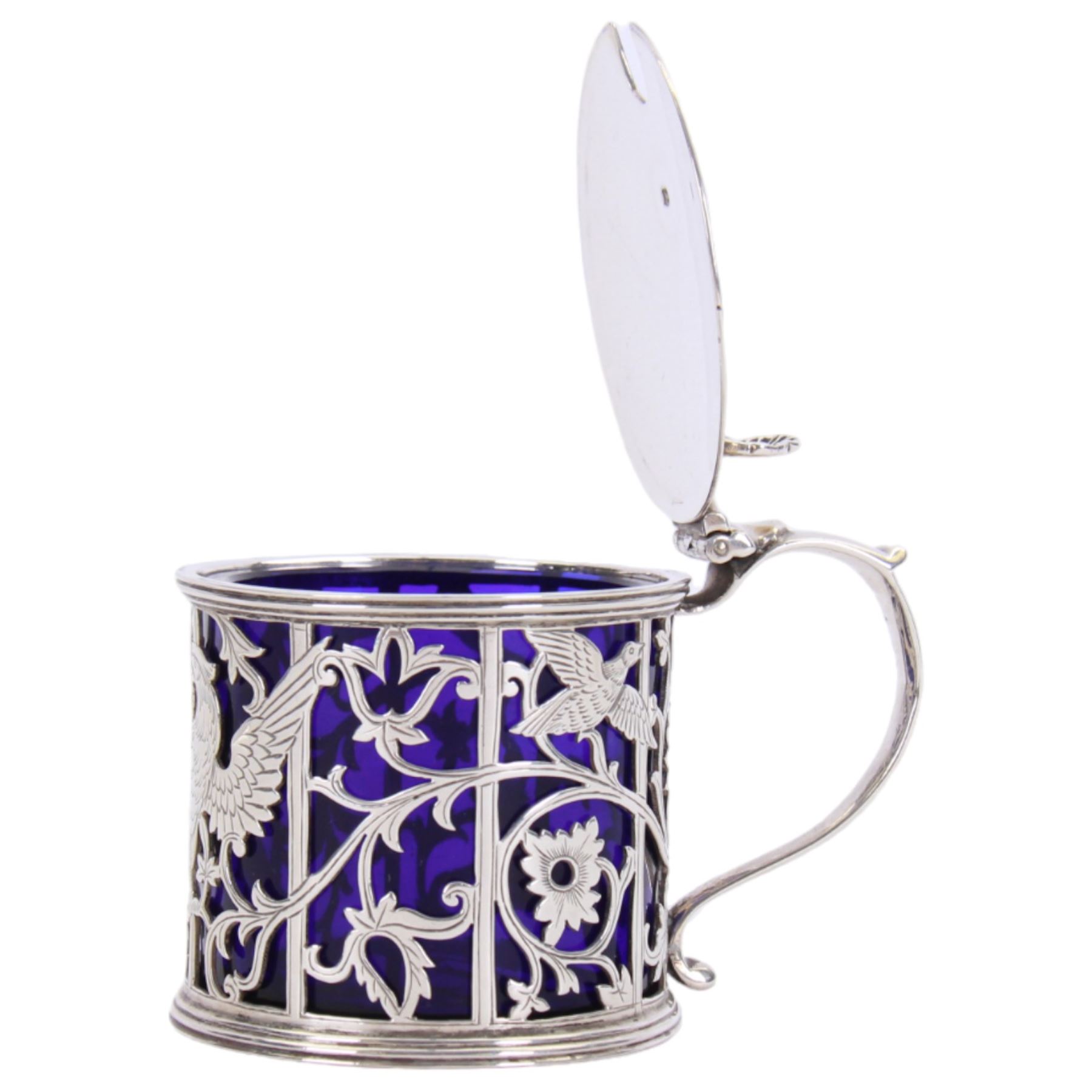 Early 20th century silver mustard pot and cover, of drum form the sides pierced with hound and birds in flight against leafy vines, the plain flat topped hinged cover with shell thumb piece opening to reveal a removable blue glass liner, hallmarked Joseph Rodgers & Sons, Sheffield 1929, including thumb piece H7cm
