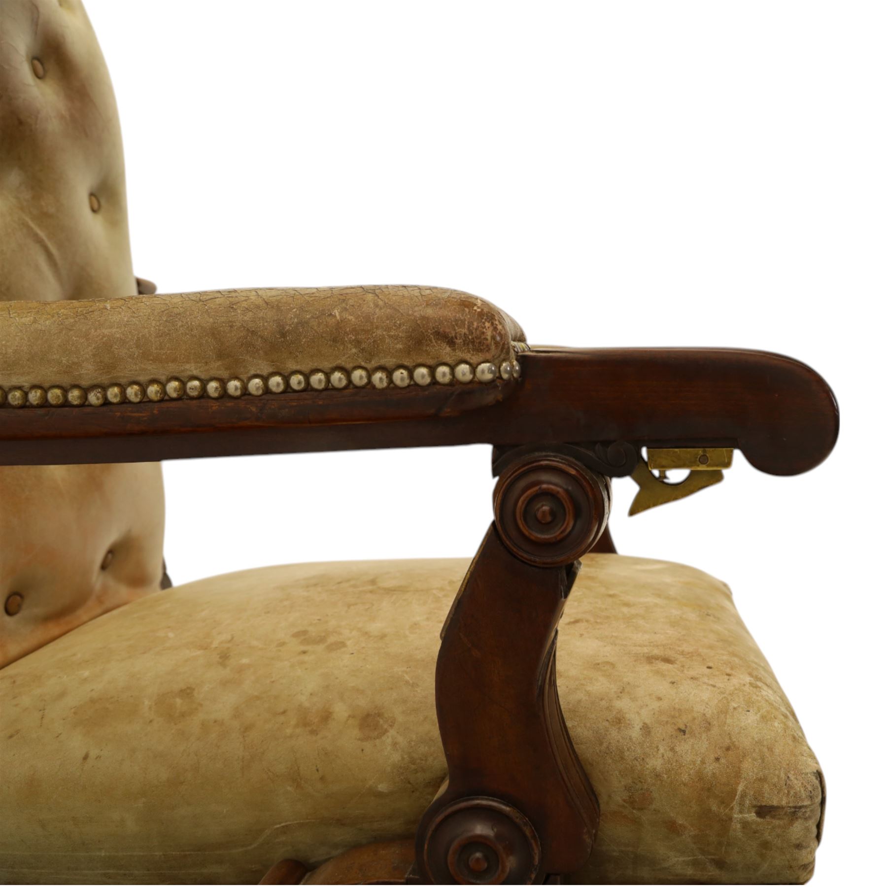 William IV mahogany gentleman's library reclining armchair, leather button upholstered and brass-studded back and seat, above leather-covered arms terminating with carved roundels and foliate scroll-carved ends, underside with brass mechanical trigger reclining lever, the apron with retractable foot rest, supported on lappet carved and turned legs with brass castors, circa 1835